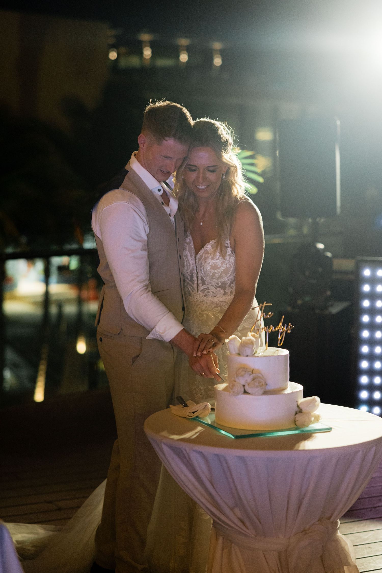Couple cutting their wedding cake together at nighttime reception.