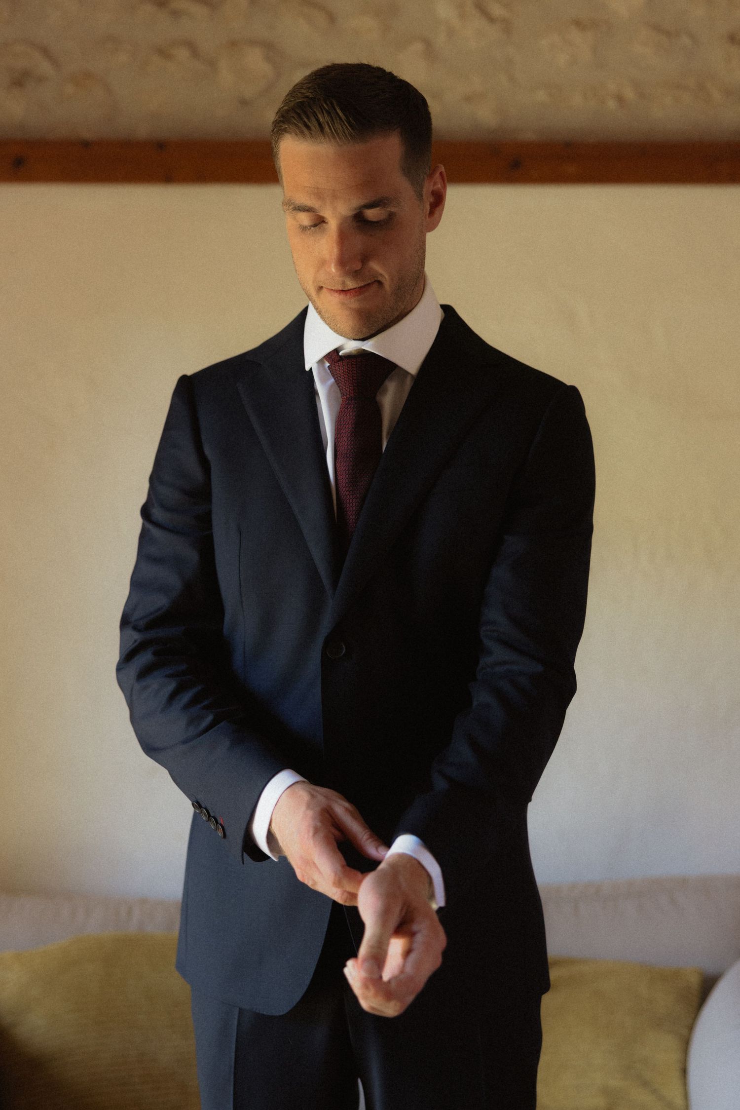Close-up shot of a man in a dark suit adjusting his tie before a formal event.