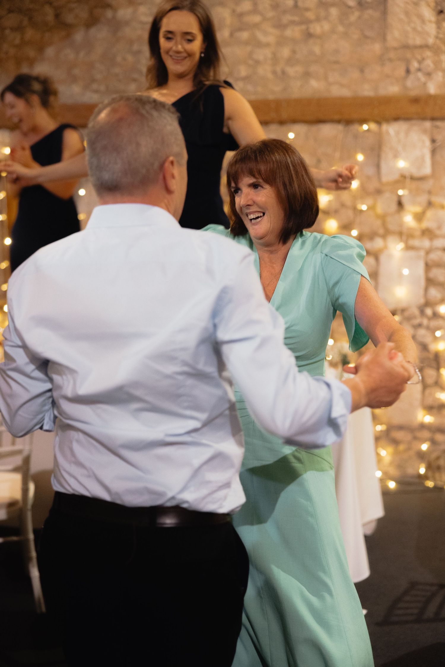 Couples dance together at wedding reception with stone walls and string lights.