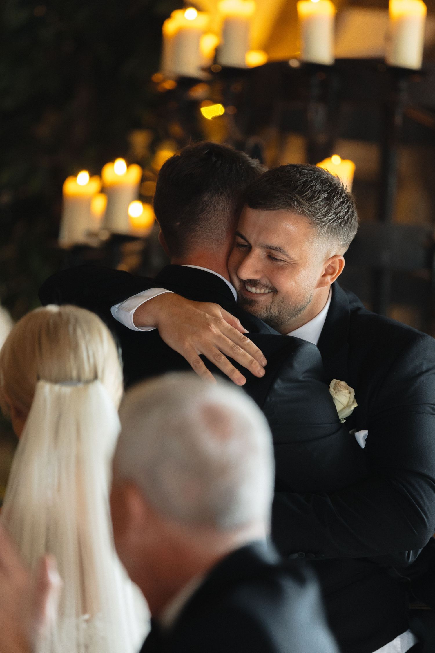 A warm embrace shared during a wedding ceremony with candlelit ambiance in the background.