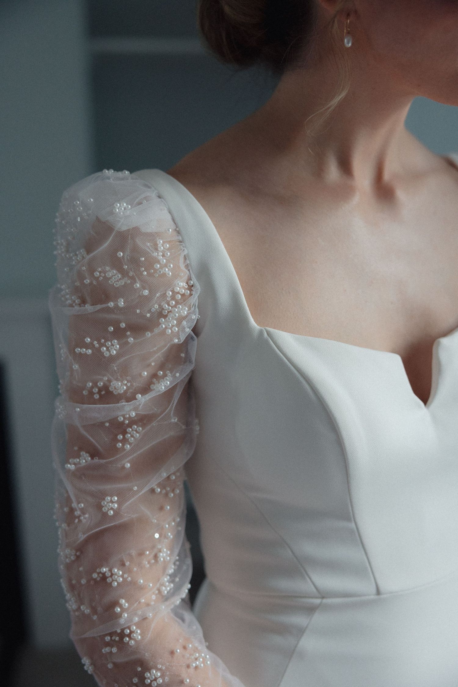 Elegant white wedding dress detail showing beaded sheer sleeves and structured bodice.