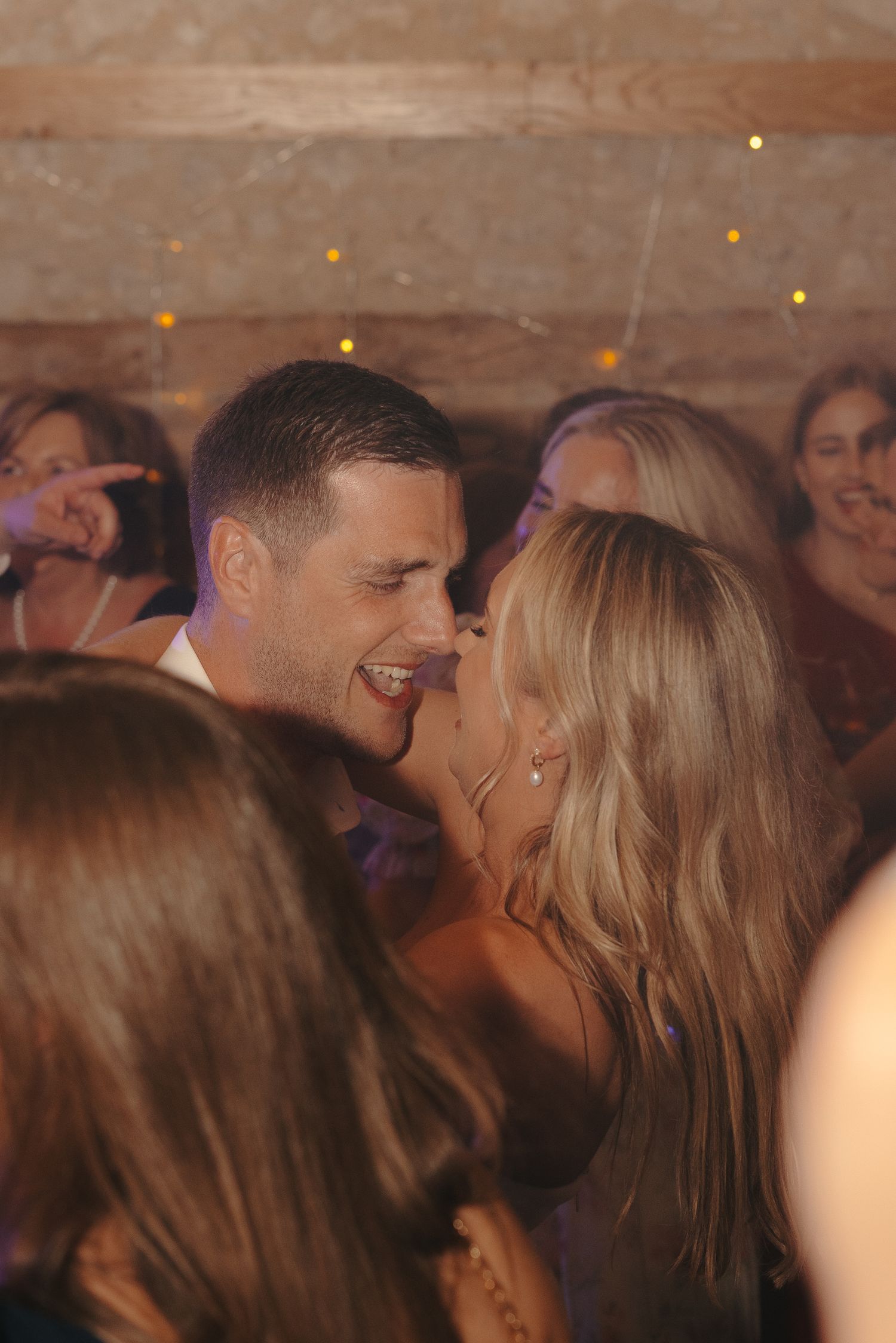 Guests dancing and celebrating at a lively wedding reception with string lights overhead.
