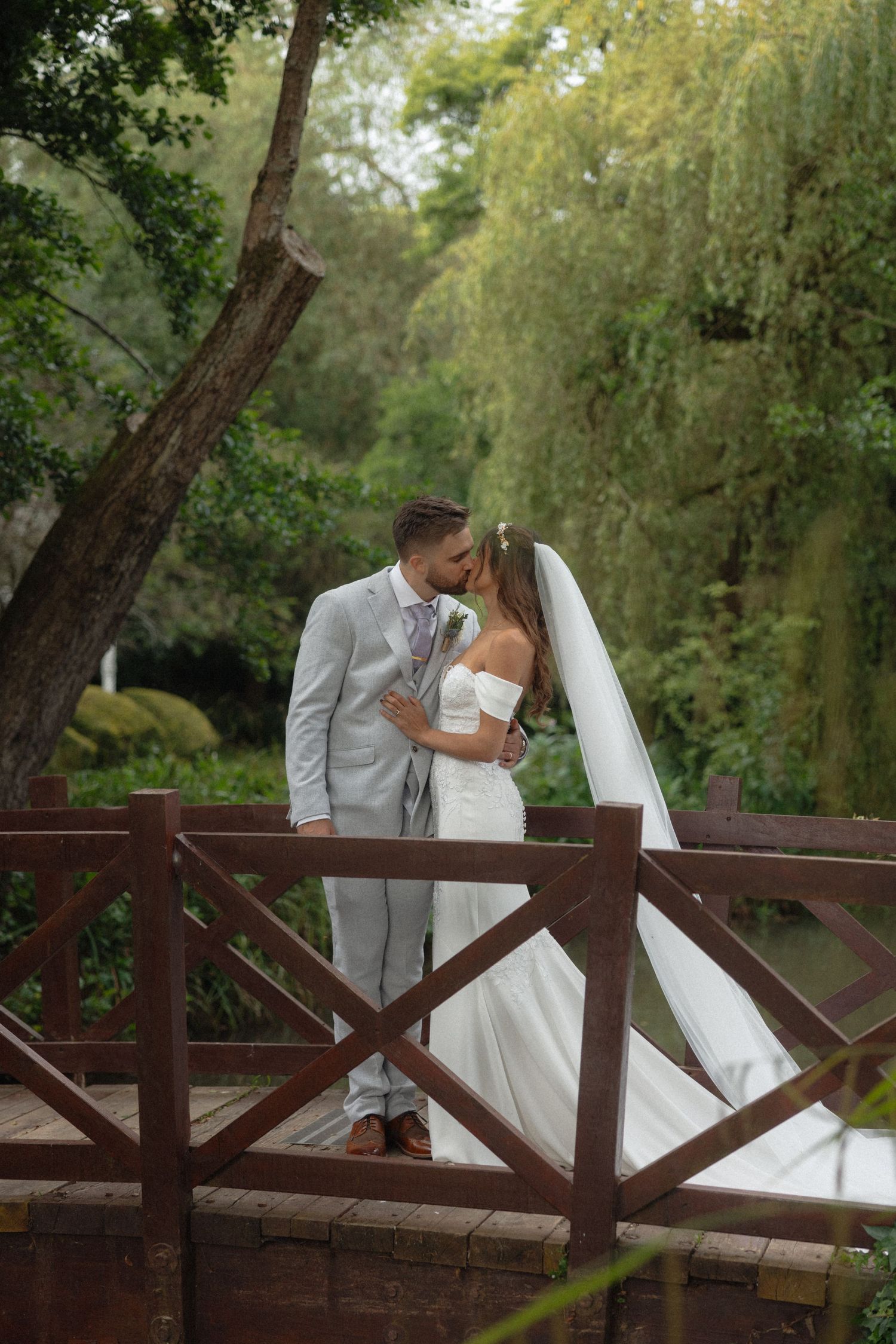 A romantic wedding moment captured on a wooden bridge surrounded by lush greenery.