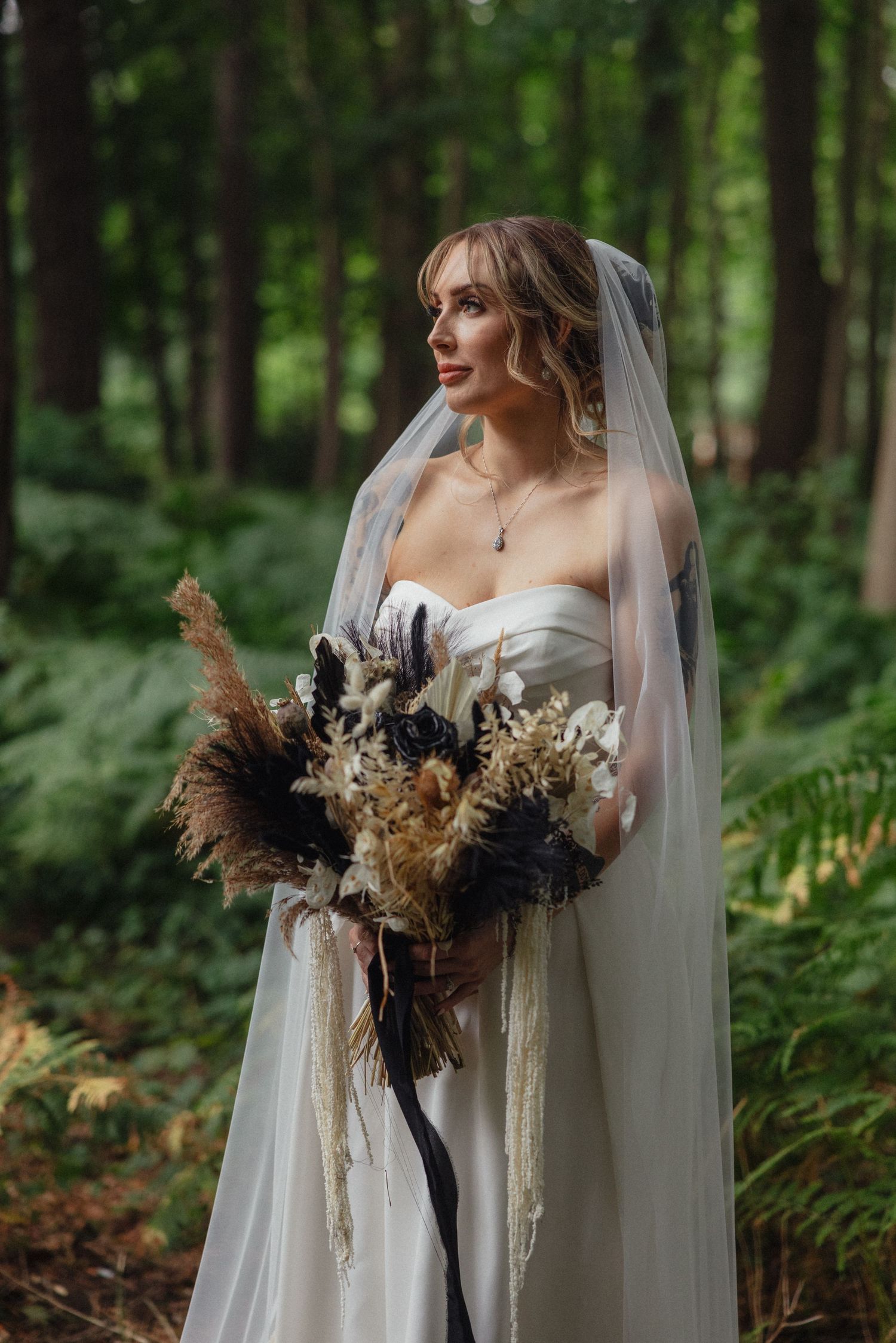 Bride holding a dramatic dried flower bouquet in a lush forest setting.
