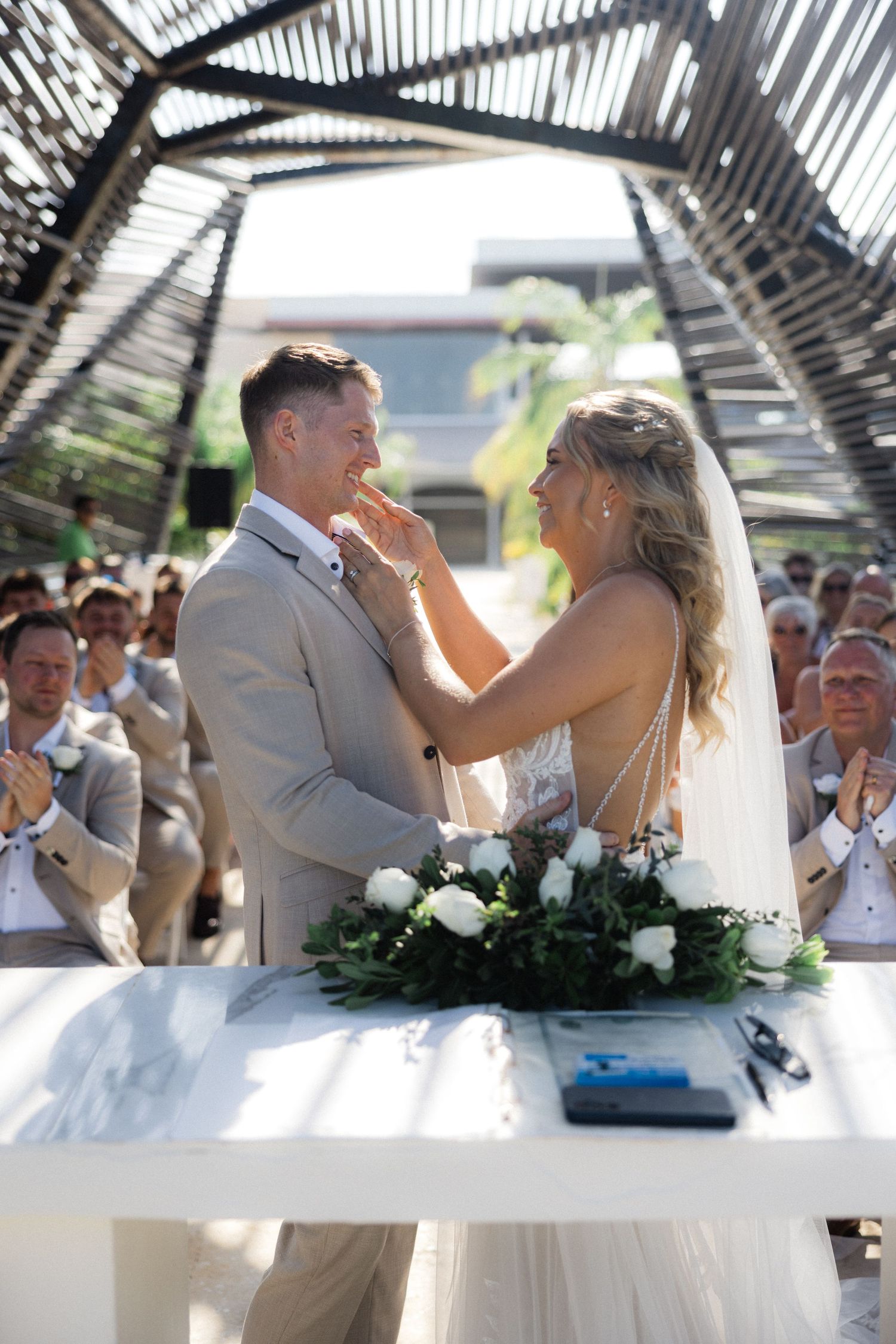 Newlyweds share their first dance under a covered pavilion at a tropical beach wedding celebration.