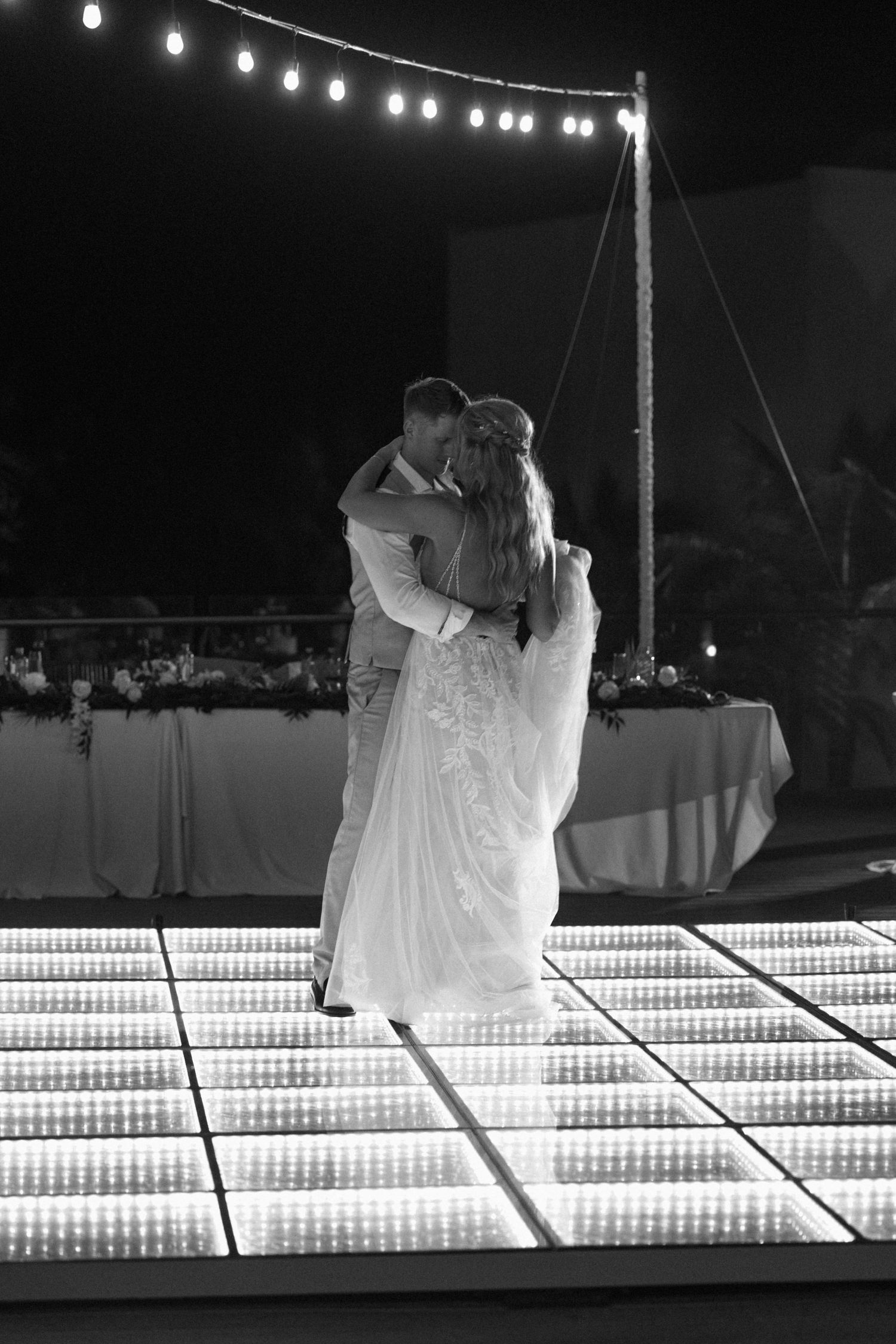 Newlyweds embrace while dancing on a glowing LED dance floor during their evening reception.