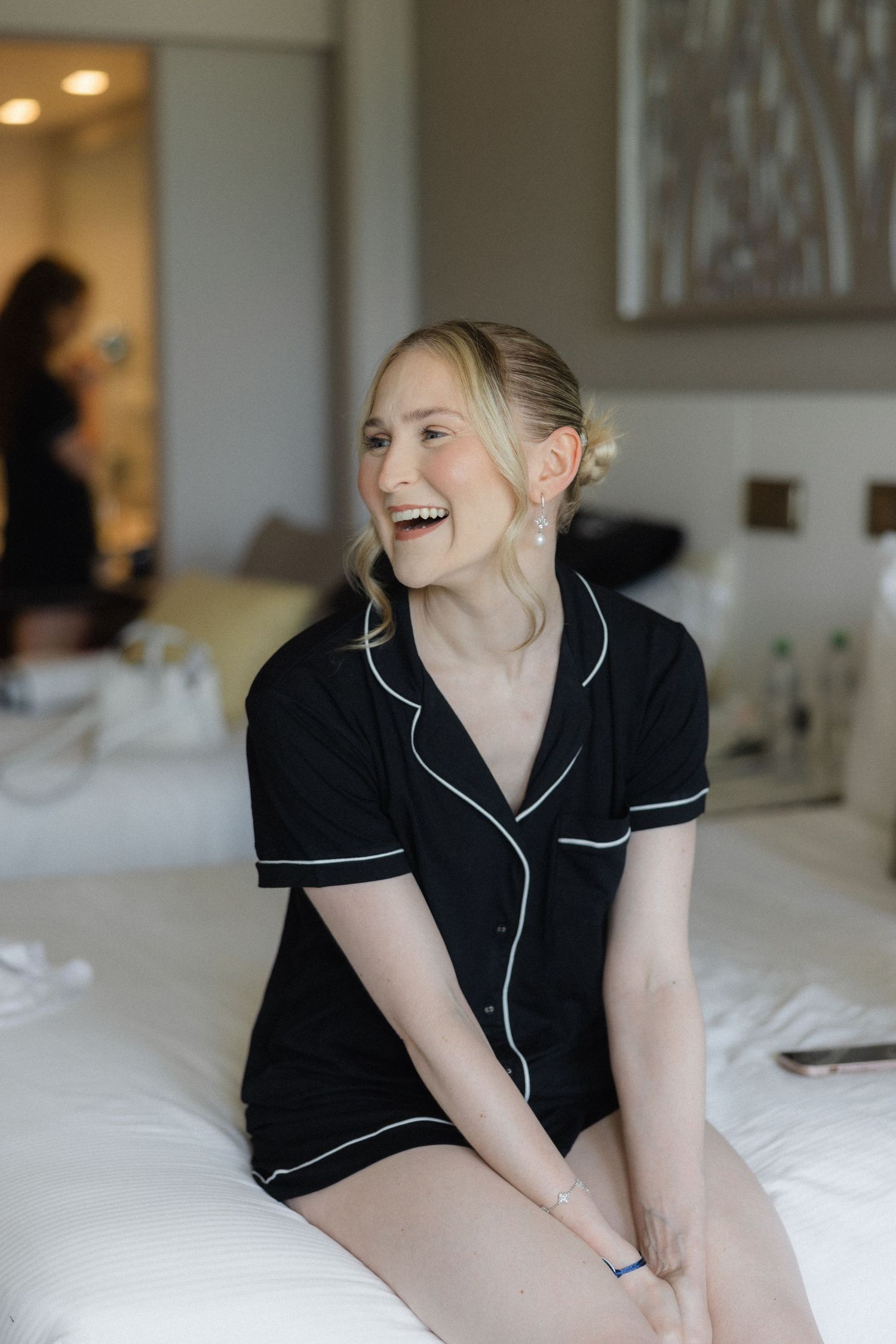 Person in black pajamas laughing while relaxing on white bedding.