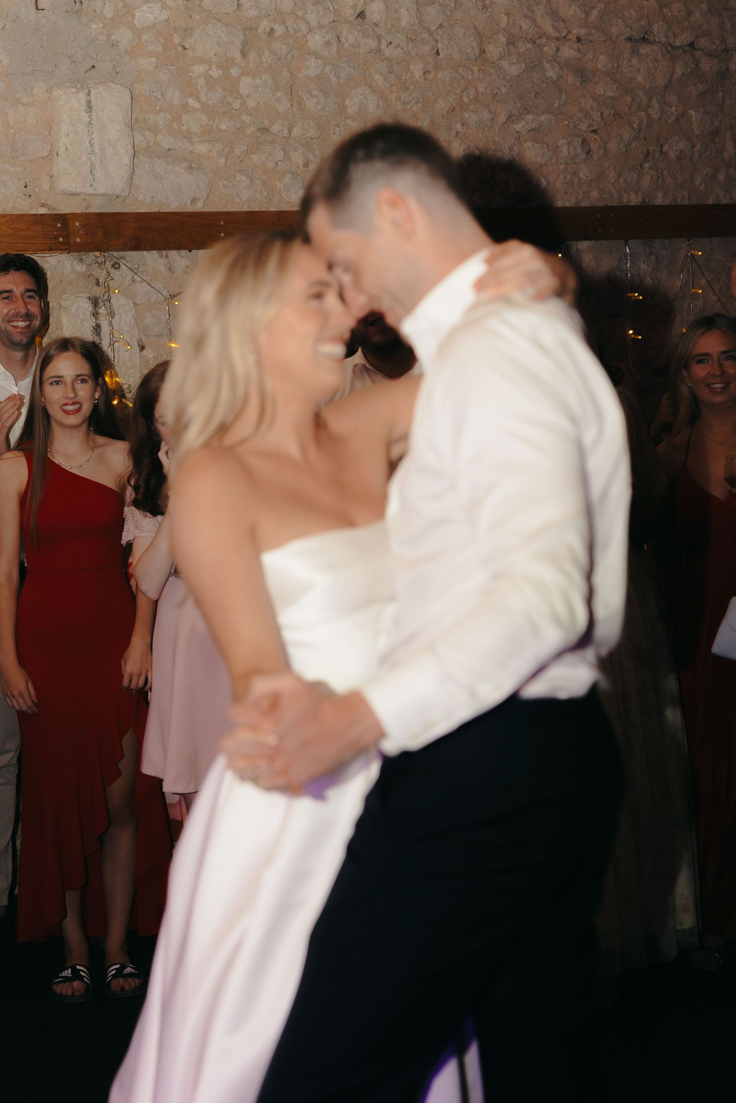Couple dancing closely at their wedding reception with guests watching in background.