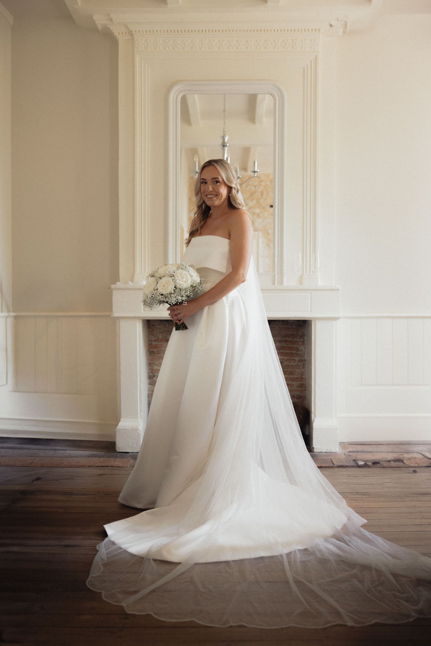 Full-length view of a flowing white wedding gown with train in an elegant room with ornate moldings.