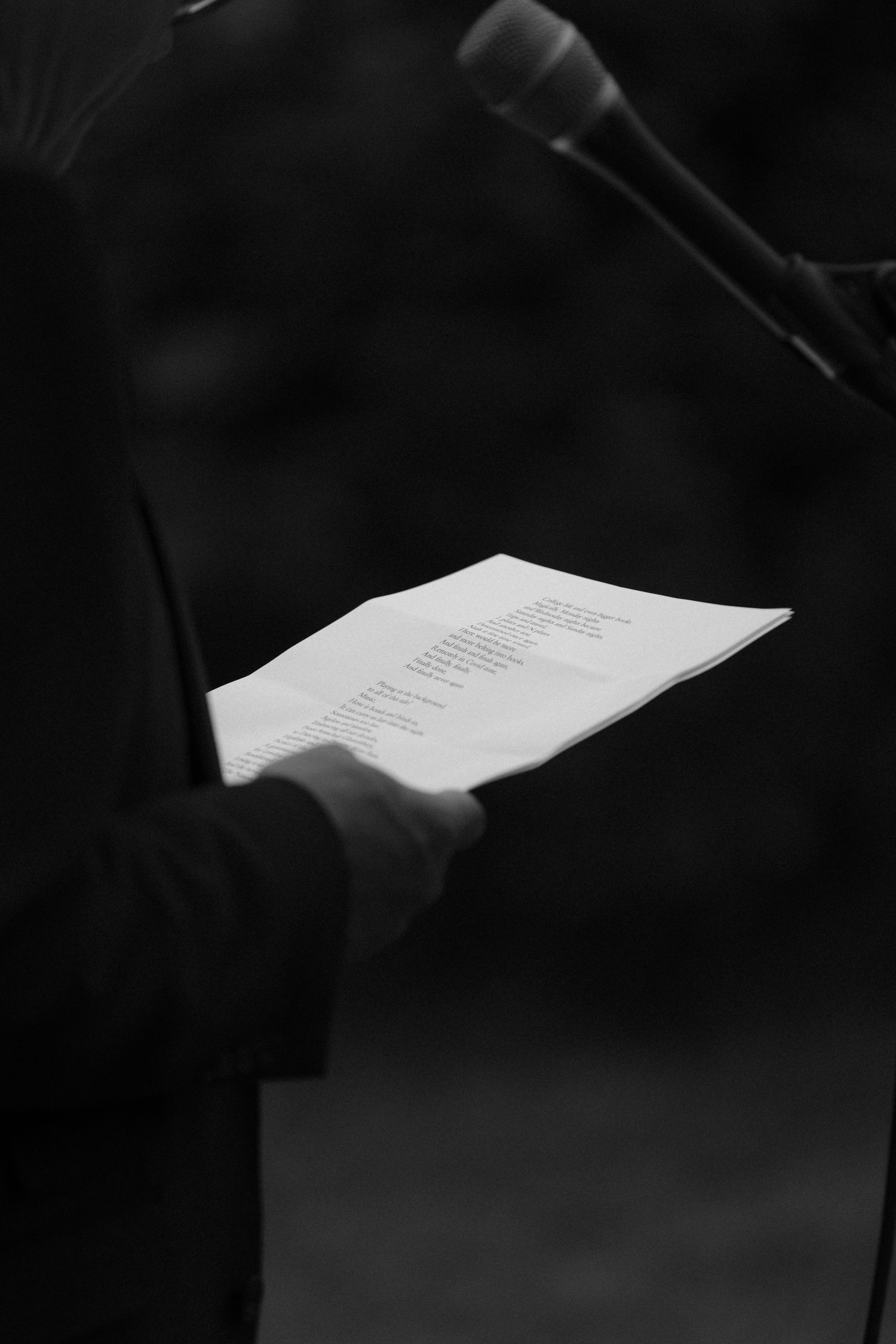 Black and white close-up of hands holding speech papers next to a microphone.