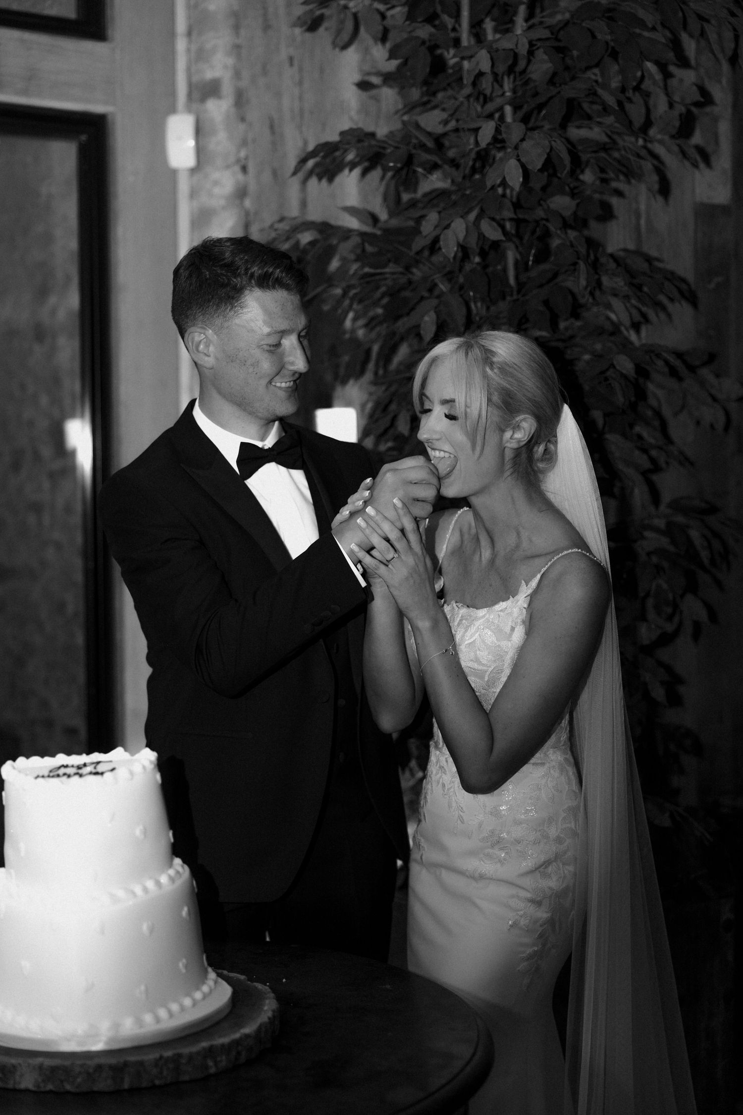 A candid black and white photo of newlyweds sharing a playful moment with wedding cake.