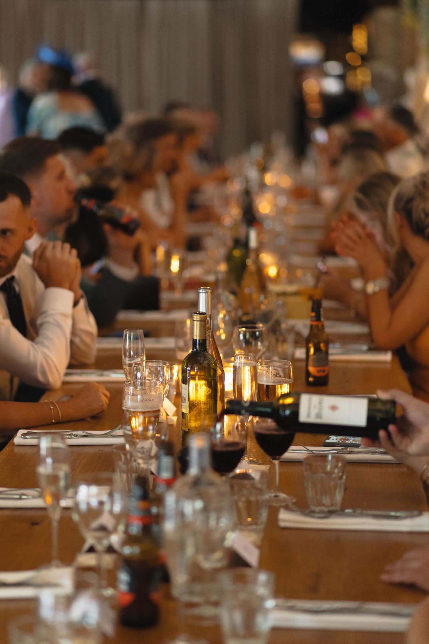 Wedding reception dinner table with wine bottles and candlelight creating an intimate atmosphere.
