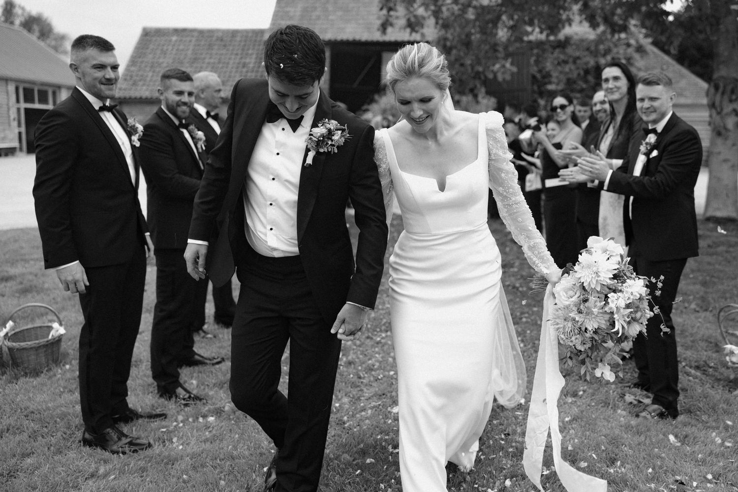 Wedding party walks together outdoors while guests throw confetti in celebration.