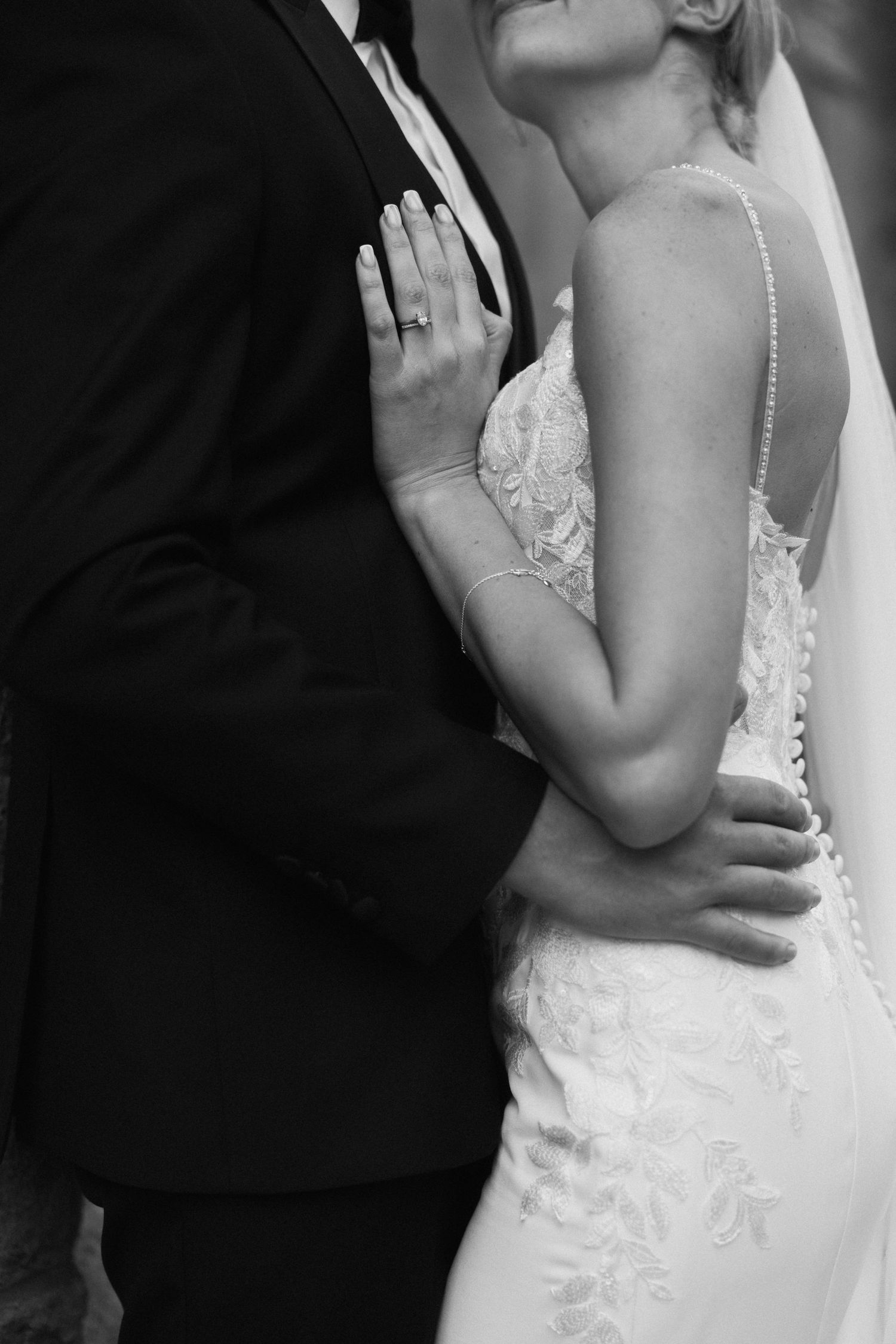 Close-up details of bride's lace dress and intimate embrace during wedding portraits.