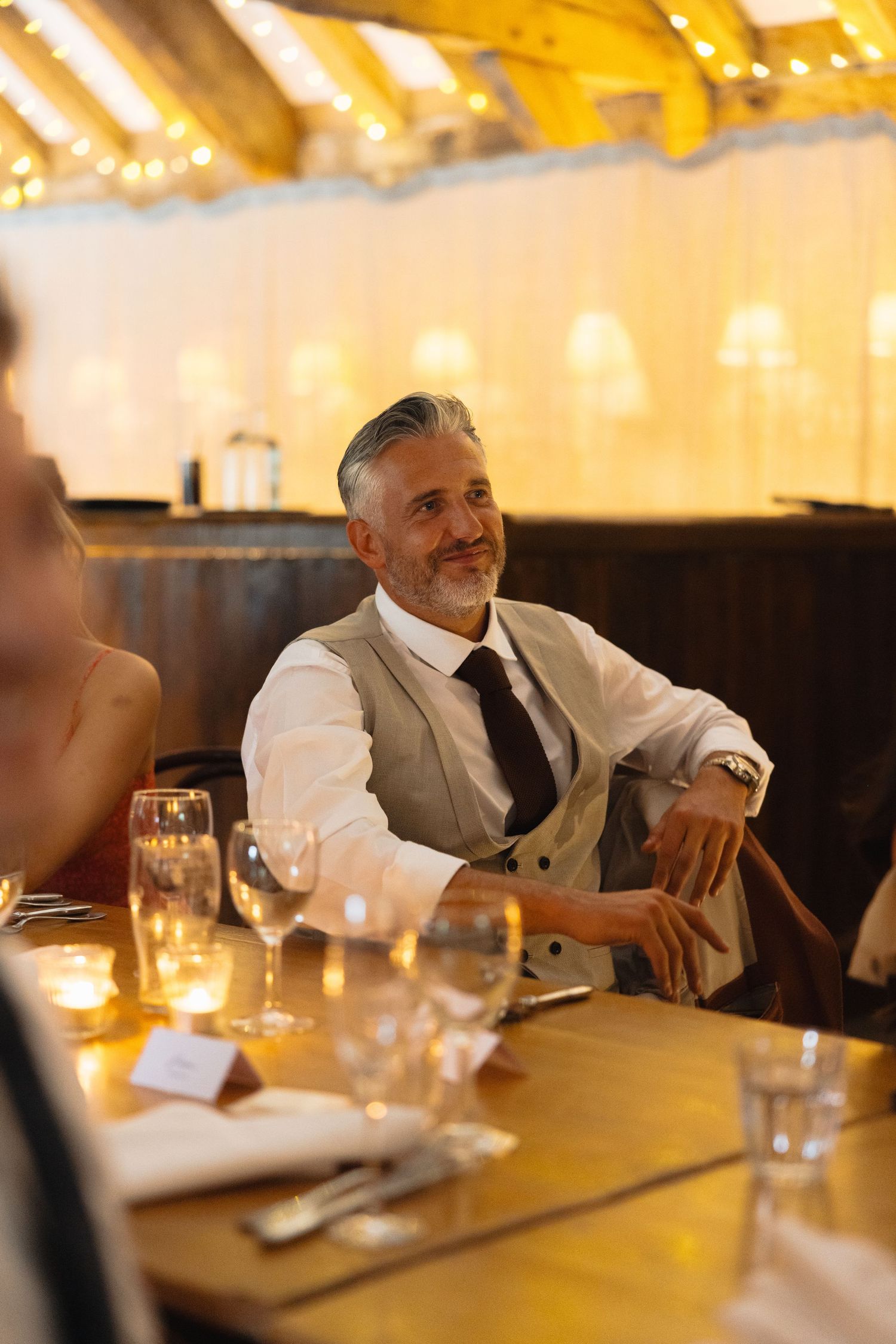 Guests share laughs at an elegant reception with warm lighting and formal table settings.