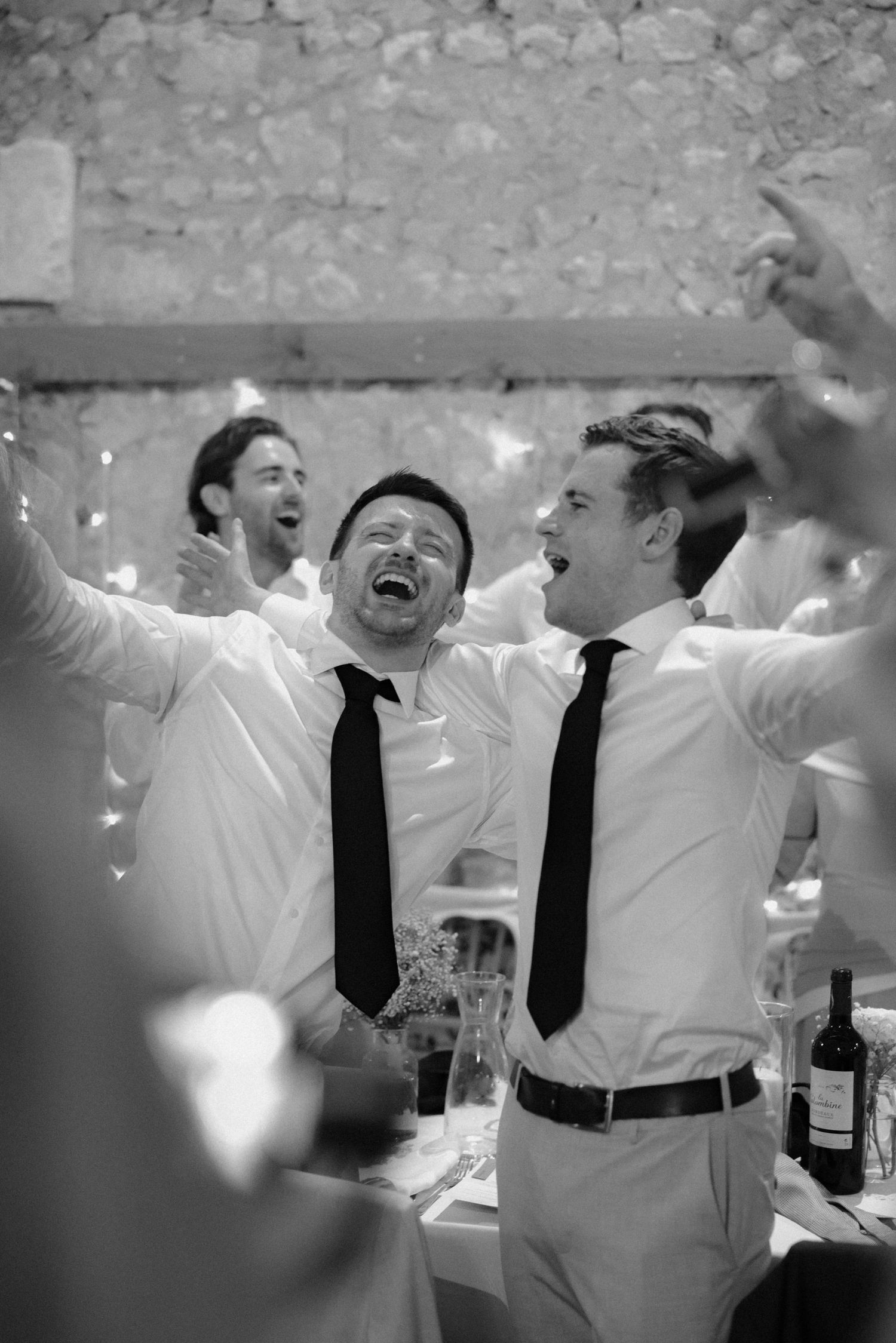 Wedding performers in white shirts and black ties celebrate energetically under string lights.