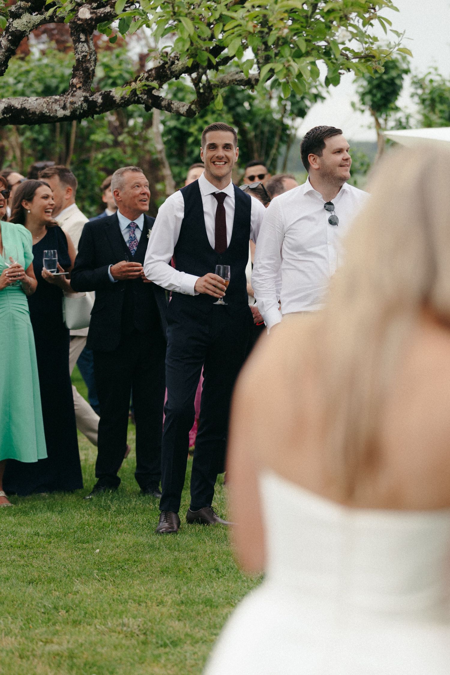 Wedding guests in formal attire gathered outdoors watching a ceremony.