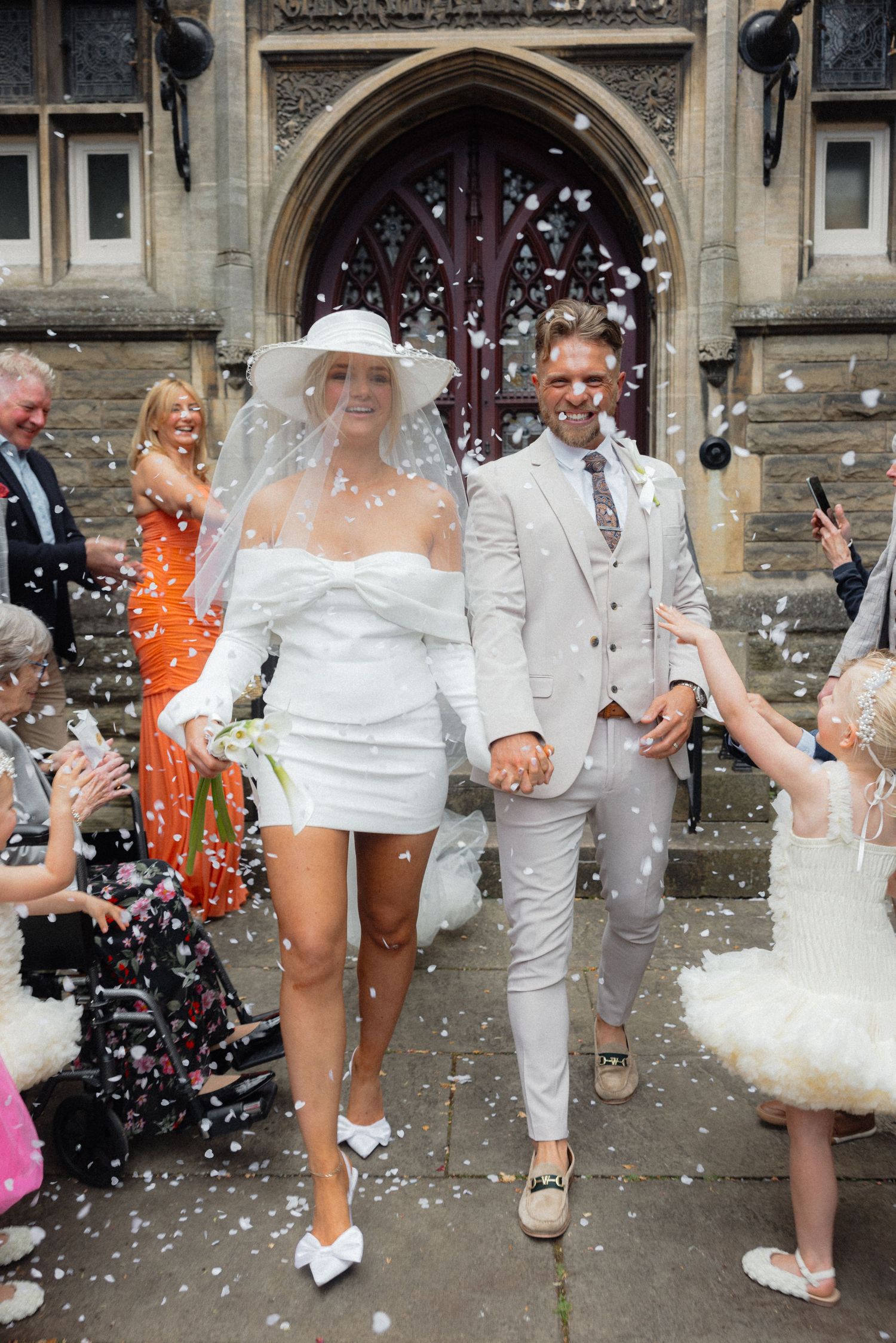 A newlywed couple exits a church while guests shower them with confetti.