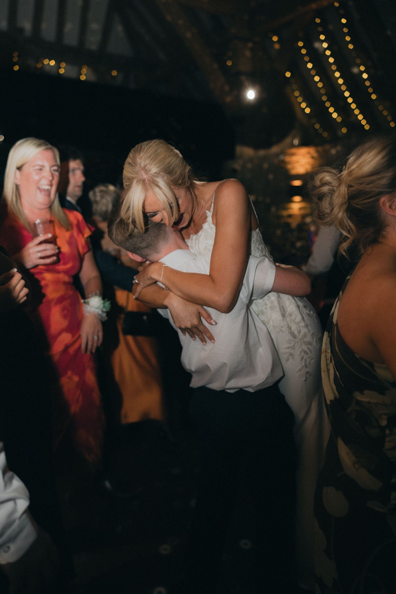 A bride dances with guests during a lively wedding reception under ambient lighting.