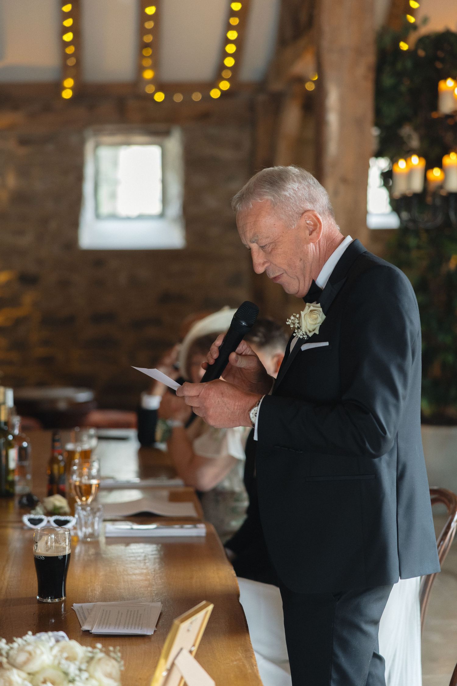 Wedding guests seated at tables in a rustic stone venue with string lights.