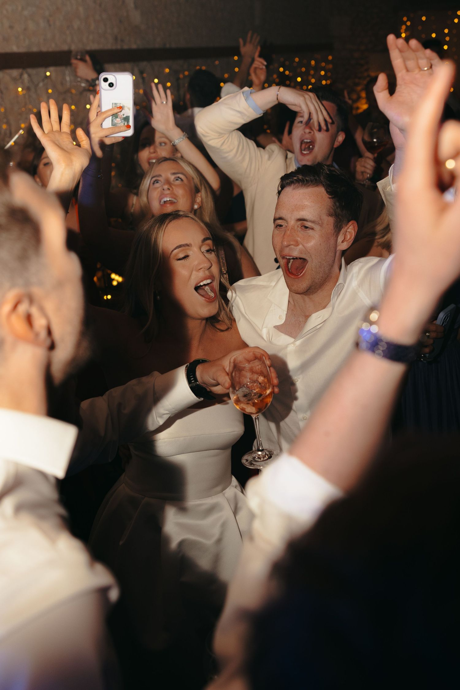 Enthusiastic wedding celebration with guests raising hands and dancing together.
