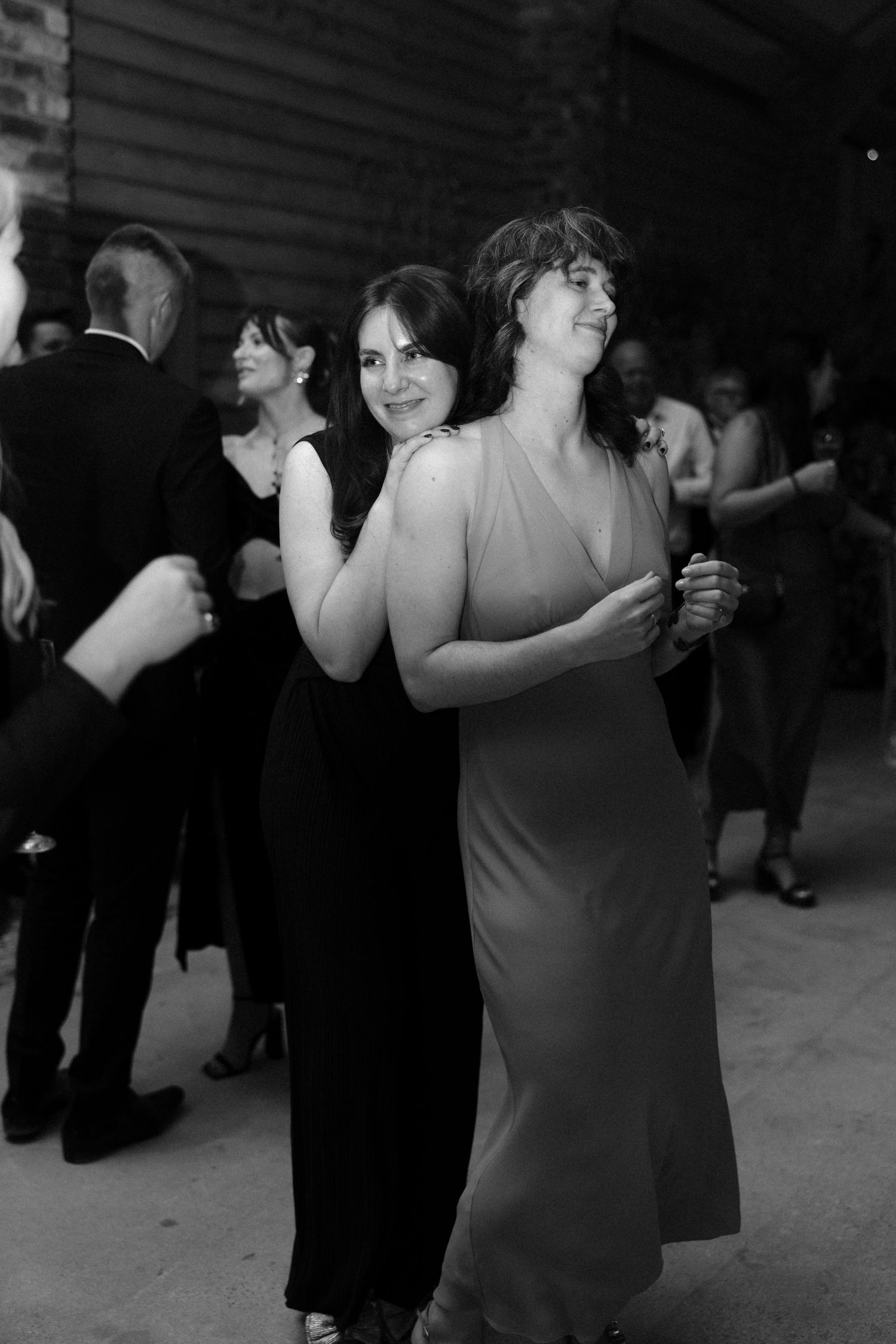Wedding guests dancing in formal attire at dimly lit reception.