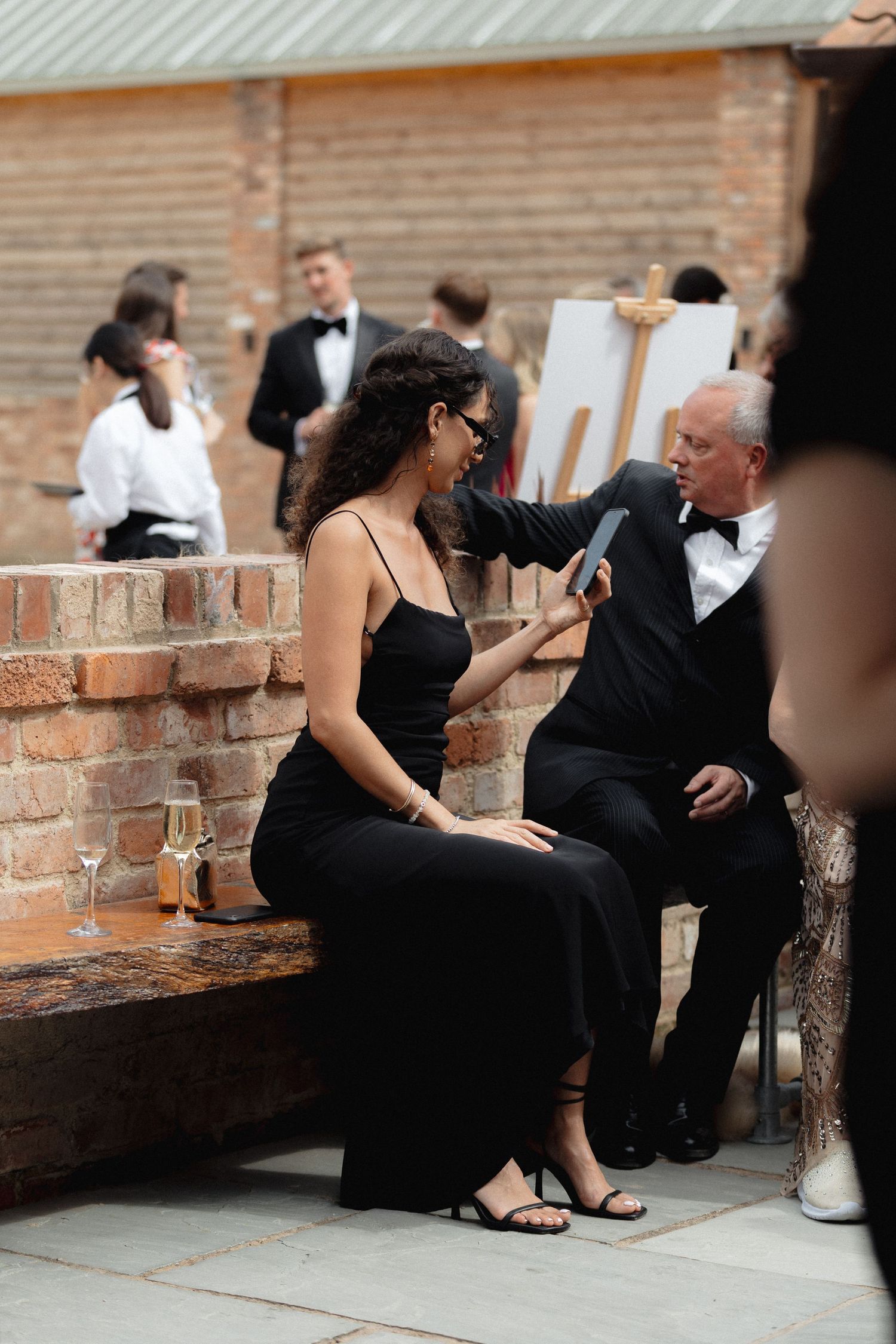 Wedding guests in formal attire relaxing on brick steps during cocktail hour.