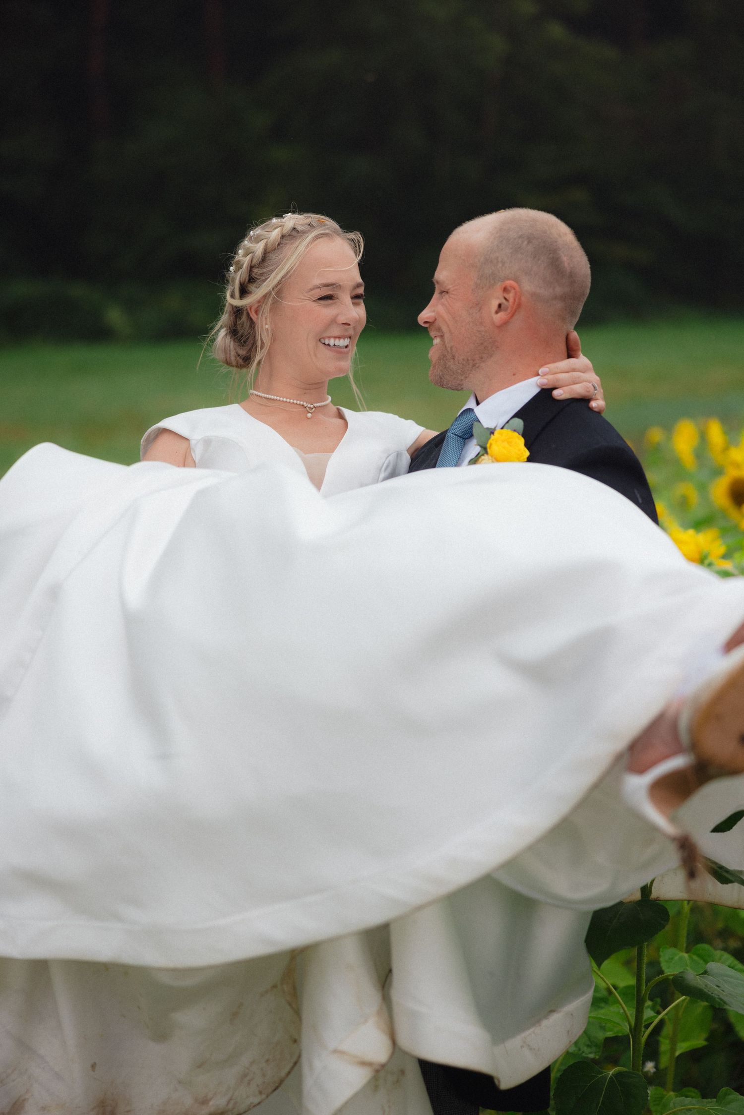 Couple spins playfully in sunflower field with flowing white wedding dress creating movement.