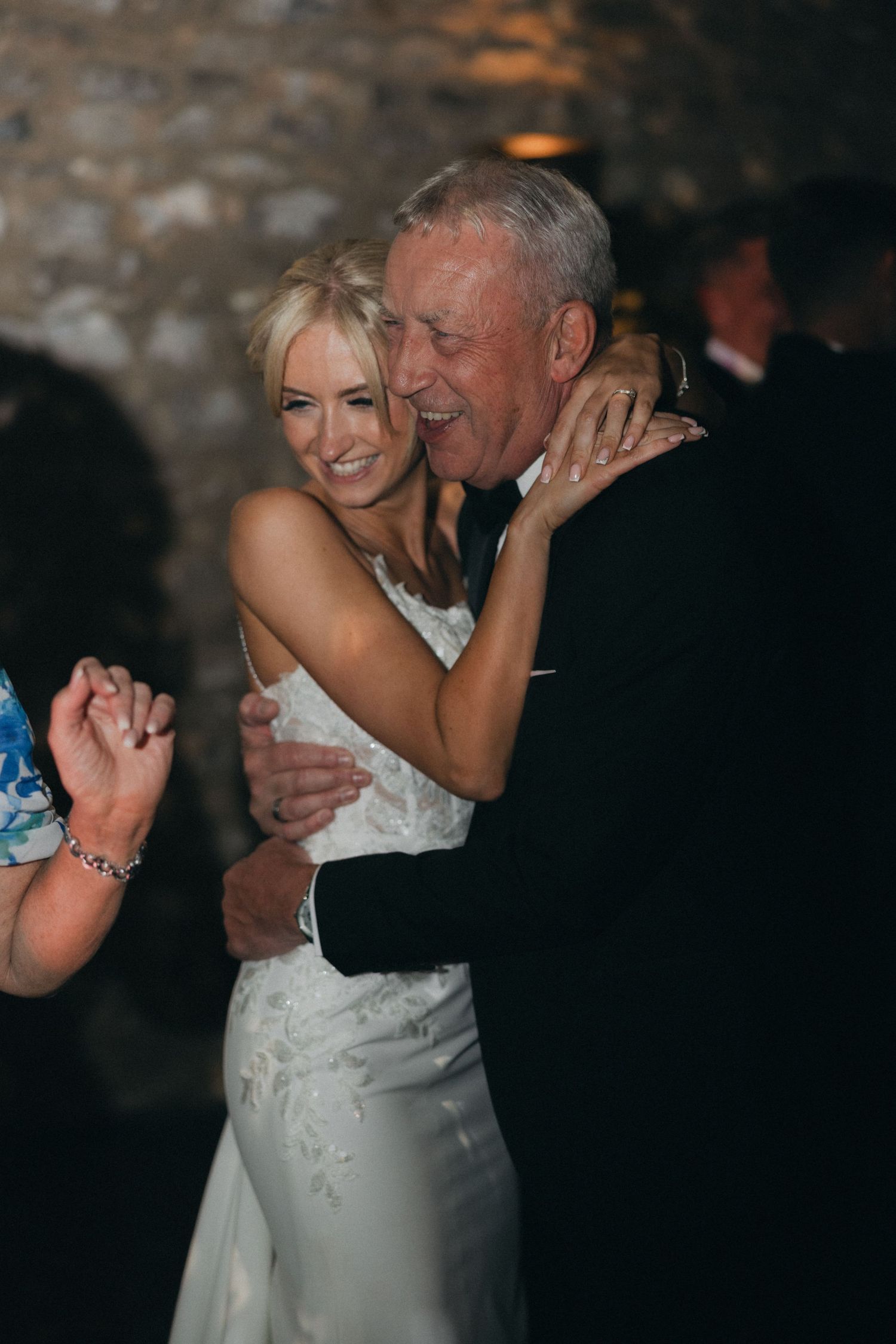 A joyful dance between a bride in a white lace dress and an older gentleman at a wedding reception.