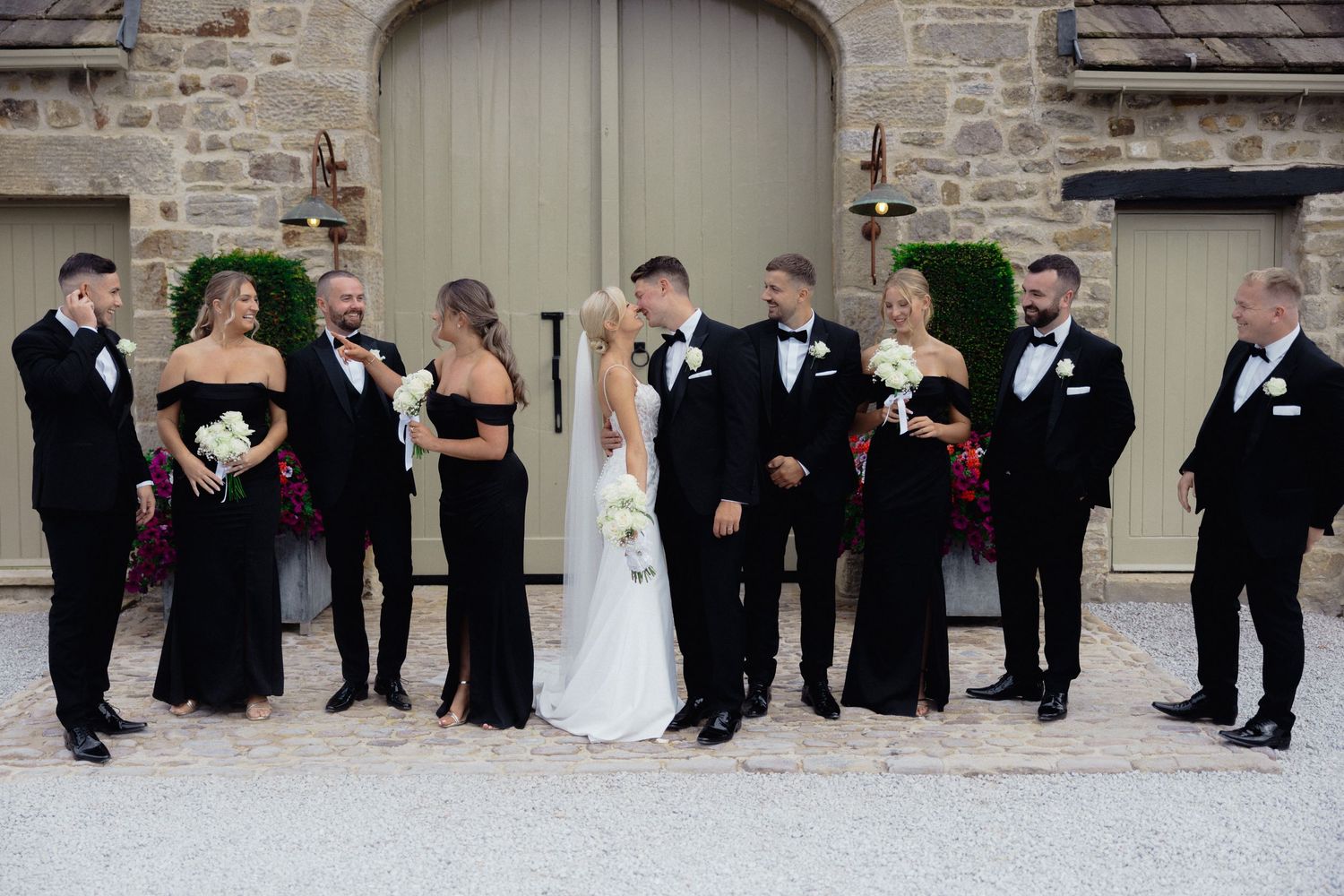 Wedding party lined up against stone wall for formal group photo.