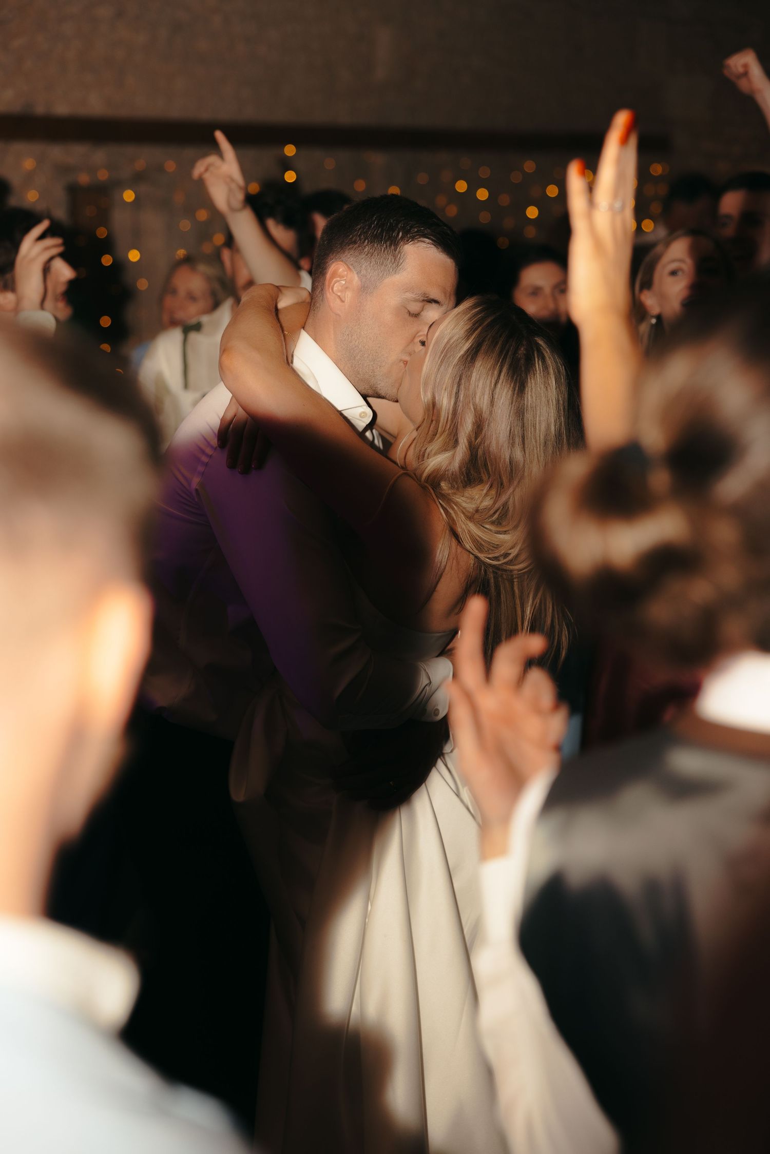 Couples dancing together at a dimly lit wedding reception with hands raised.
