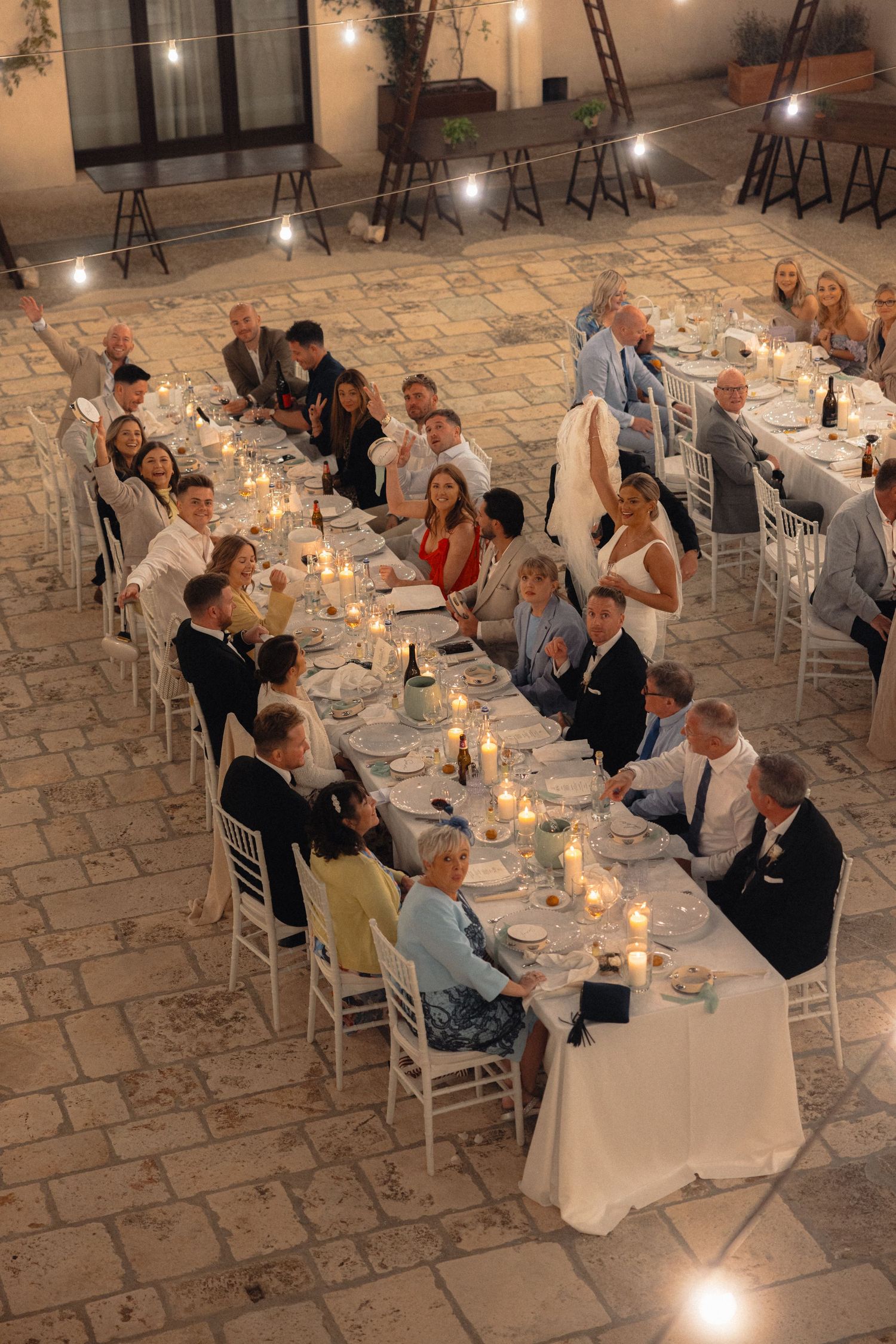 Wedding guests seated at long tables during evening reception with candlelight.