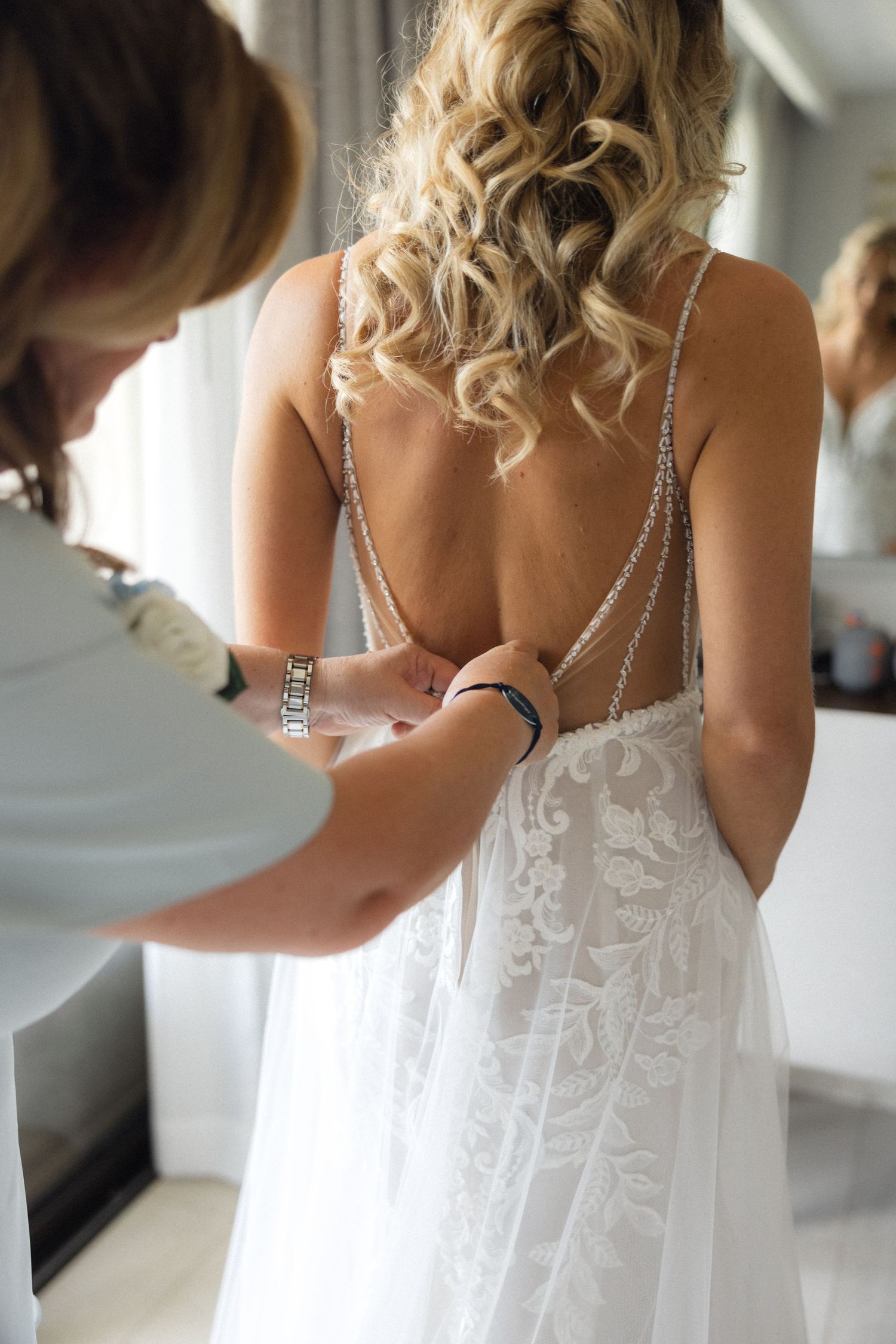 Close-up of wedding dress being buttoned up, showing delicate lace and beading details.