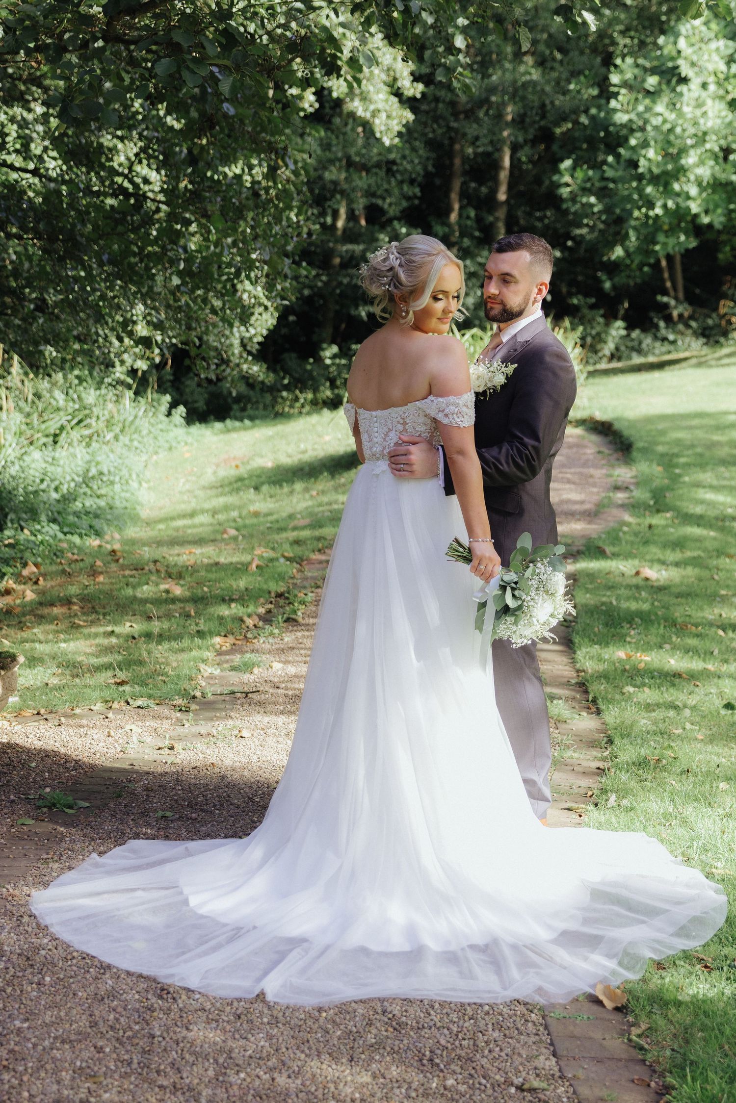 An elegant wedding portrait on a garden path with a flowing white dress and trailing veil.