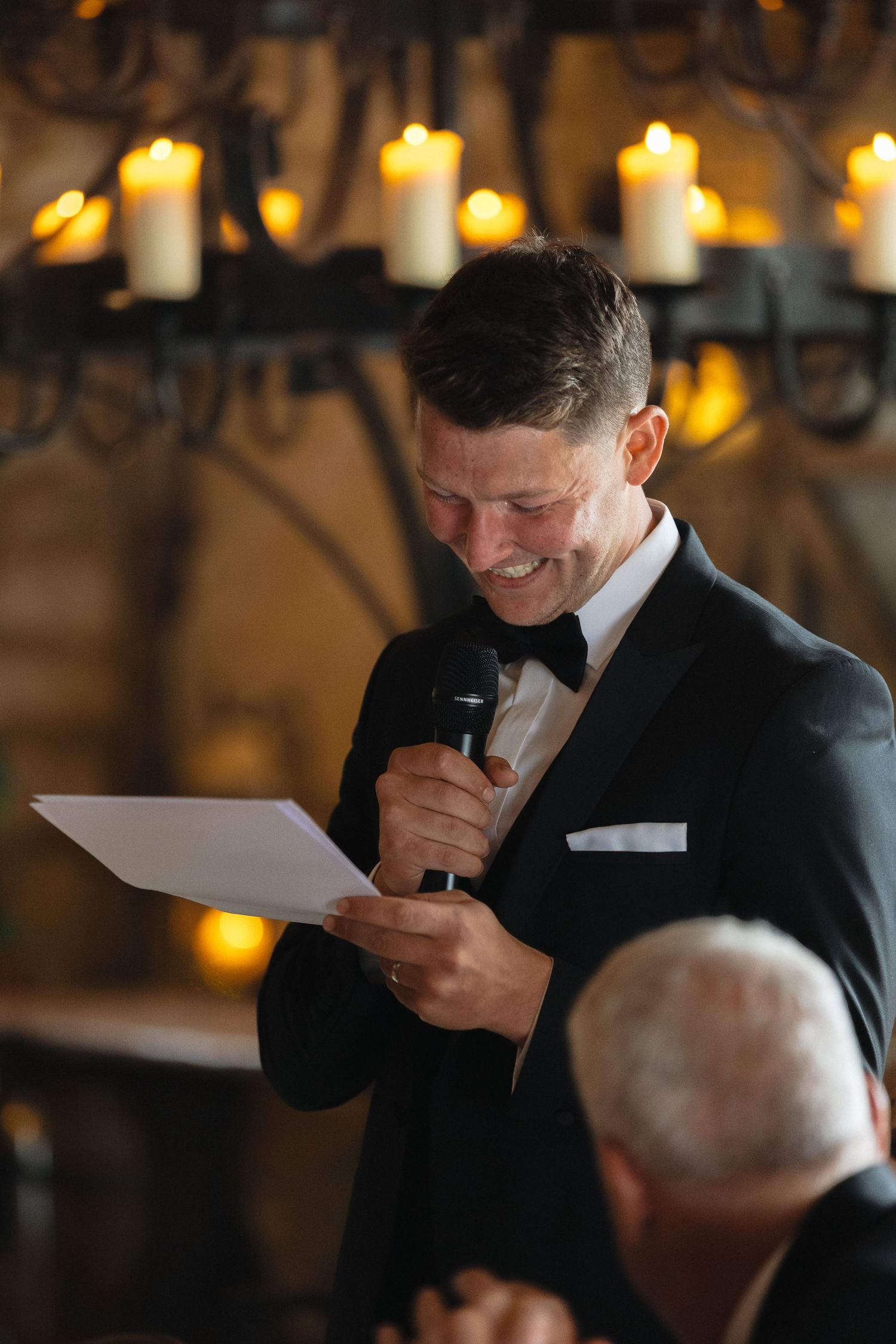 A speaker delivers an emotional speech at a formal reception with stone walls and candlelight.