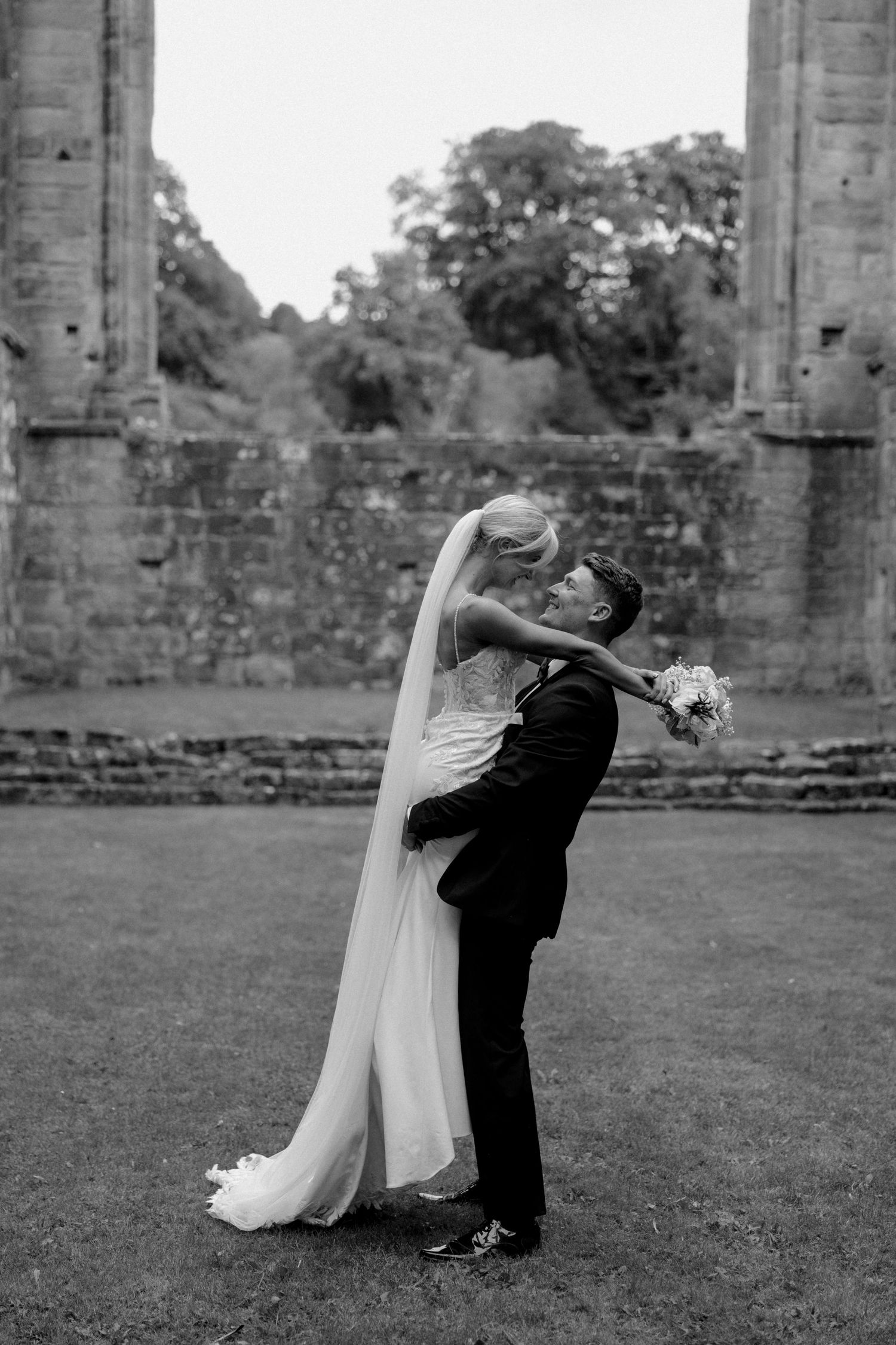 Black and white wedding photo series showing couple in dramatic dip pose near stone pillars.