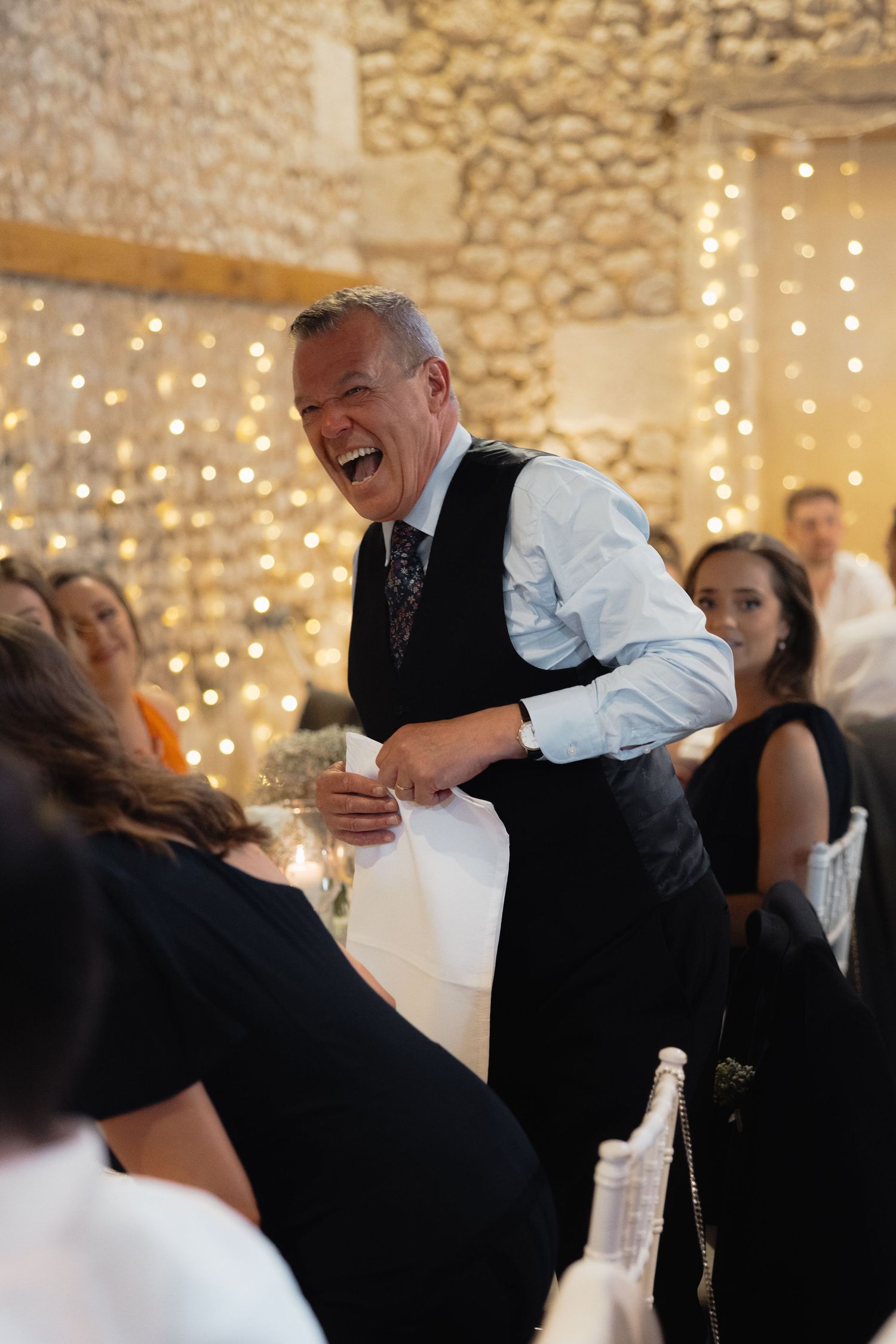 Wedding guests laugh and dance under twinkling lights in stone-walled reception venue.