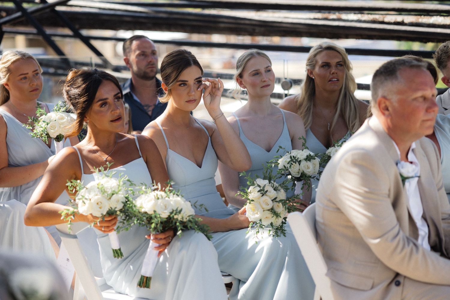 Wedding party and guests gathered under architectural pergola during ceremony.