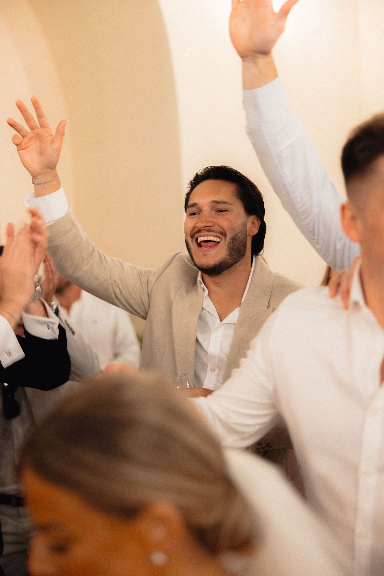 Wedding guests celebrating with raised arms in a warmly lit indoor venue.