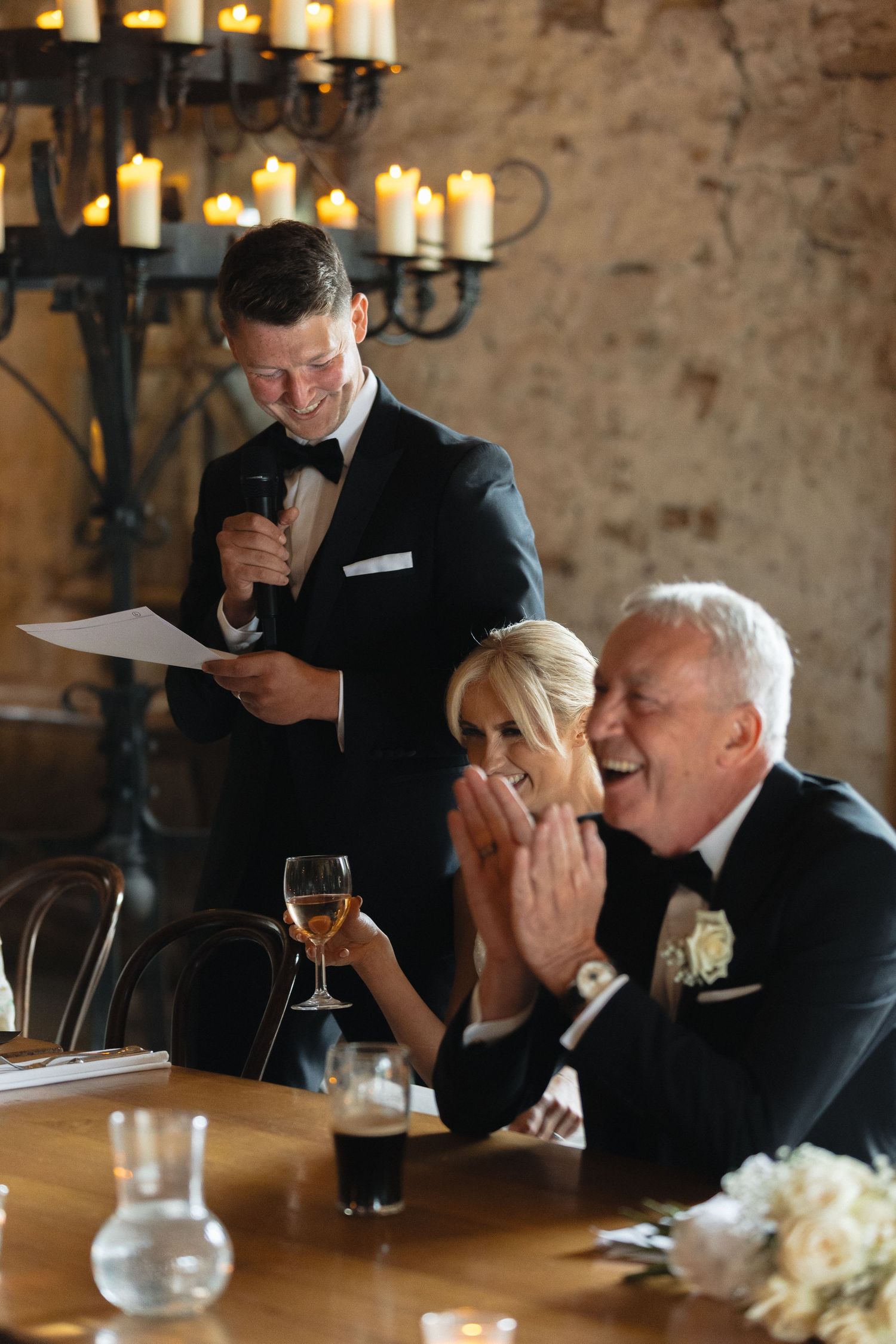 Guests in formal attire share emotional moments at an elegant reception with stone walls and candlelight.