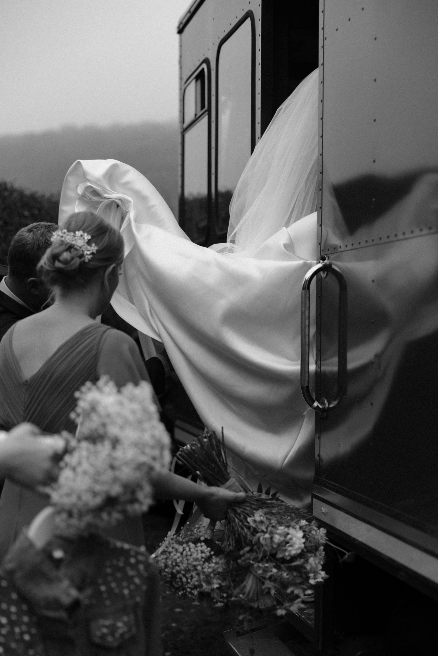 Black and white artistic photograph showing wedding veil flowing in the breeze with delicate flowers.