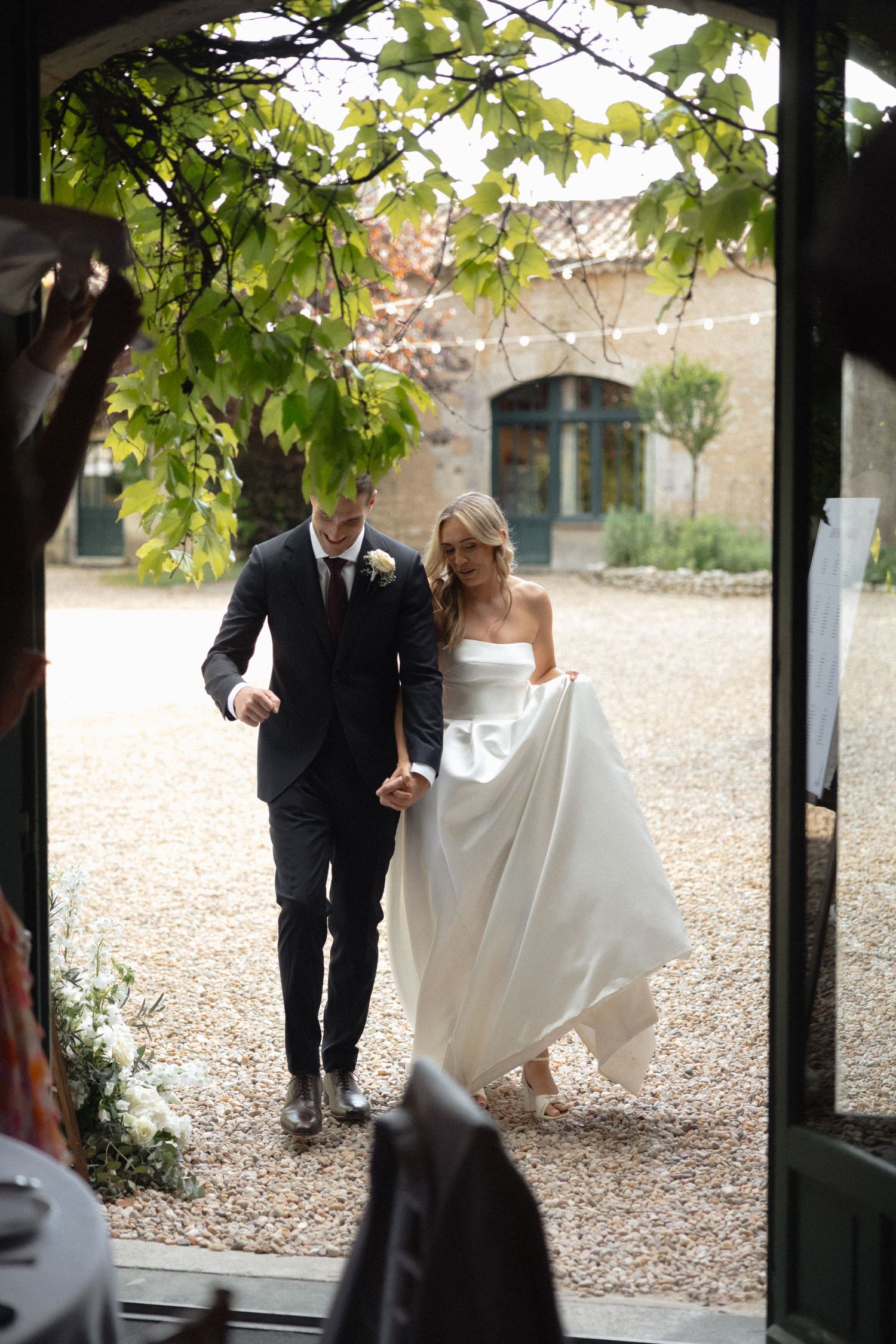 Couple walking under pergola covered with green leaves at outdoor venue.
