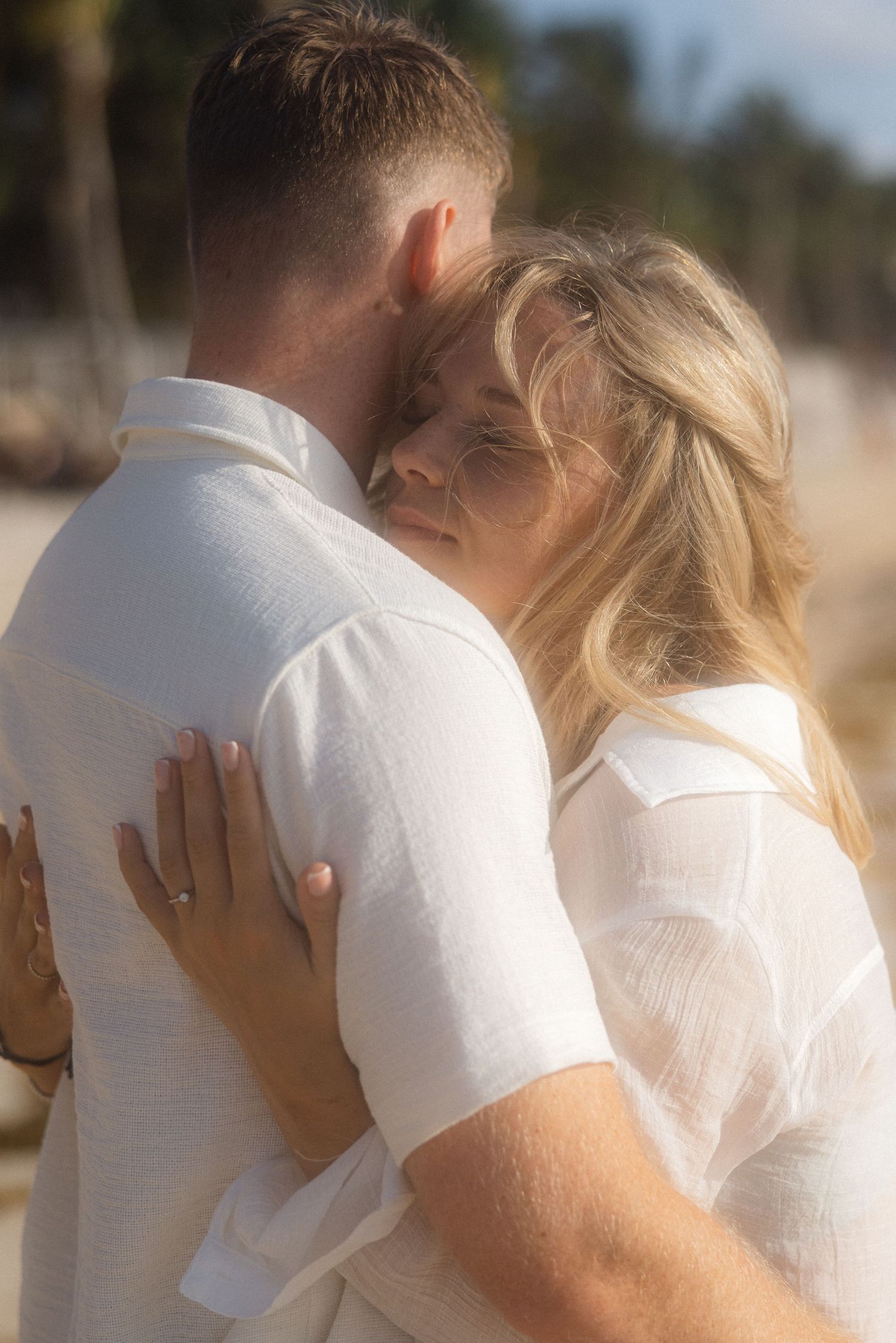 An intimate moment shared between a couple in white attire on a beach.