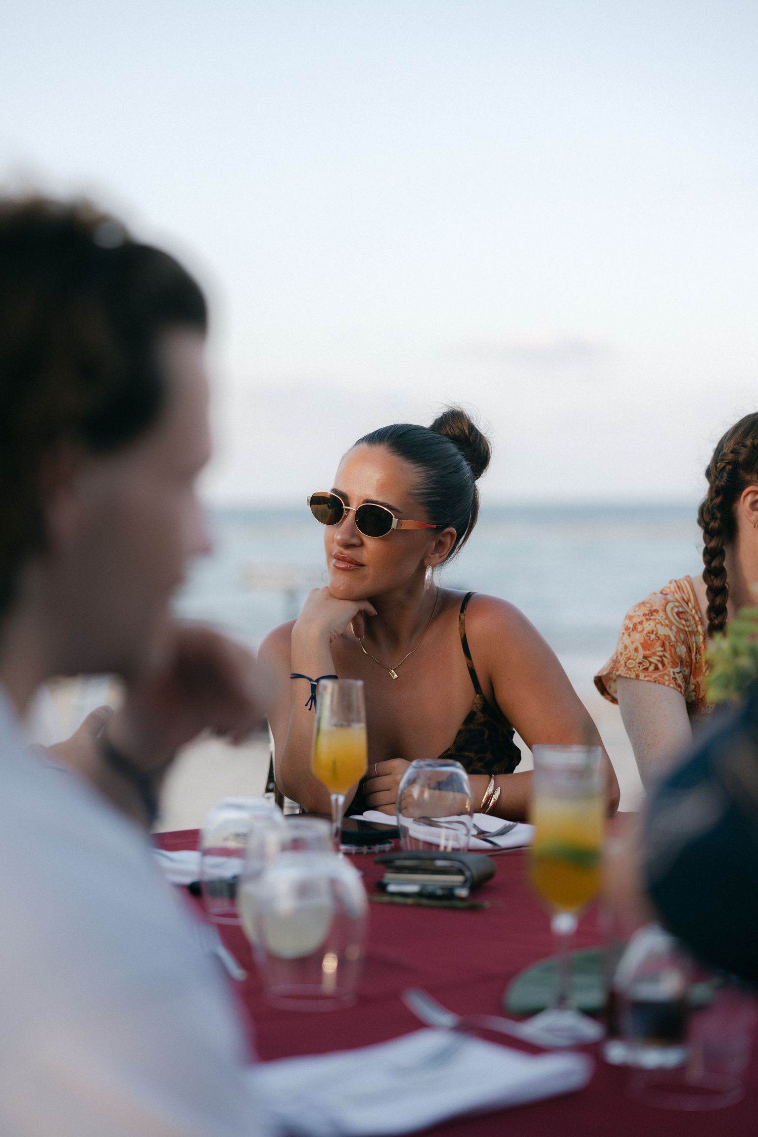 Guest in sunglasses smiling during beachside dinner conversation.