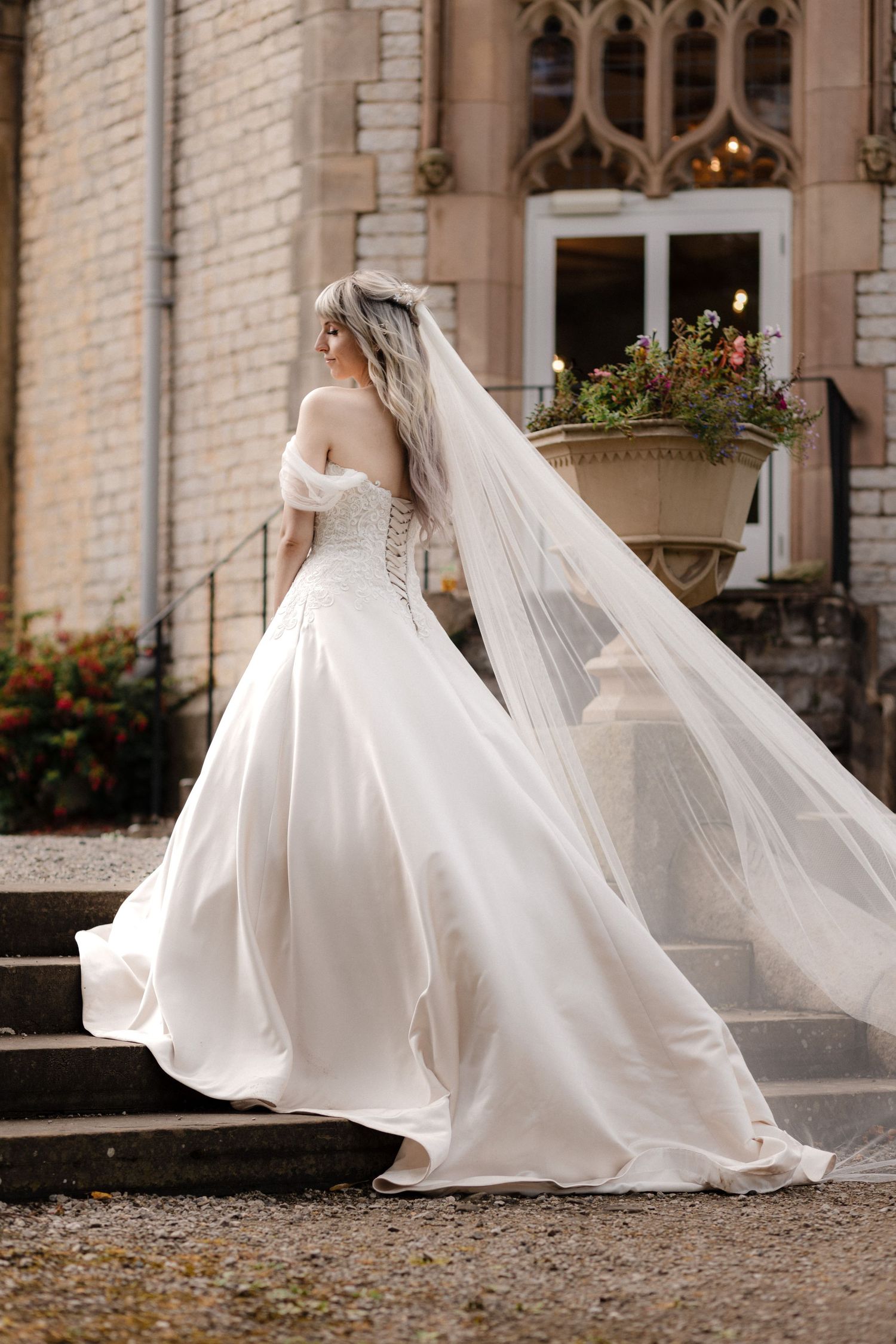 A flowing white wedding gown with a dramatic train photographed in motion against a historic brick building exterior.