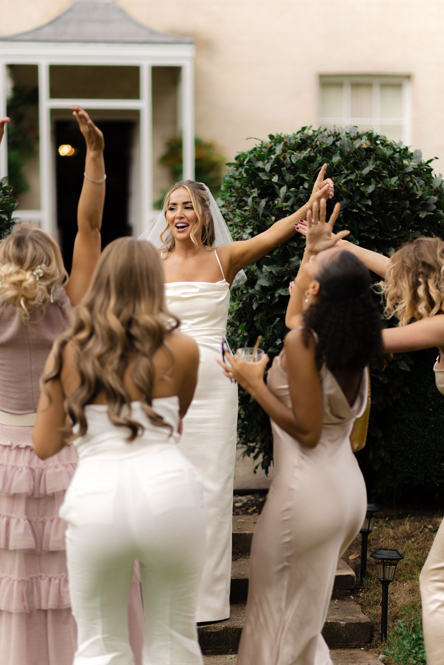 Bridesmaids in blush dresses celebrating joyfully outside a wedding venue.