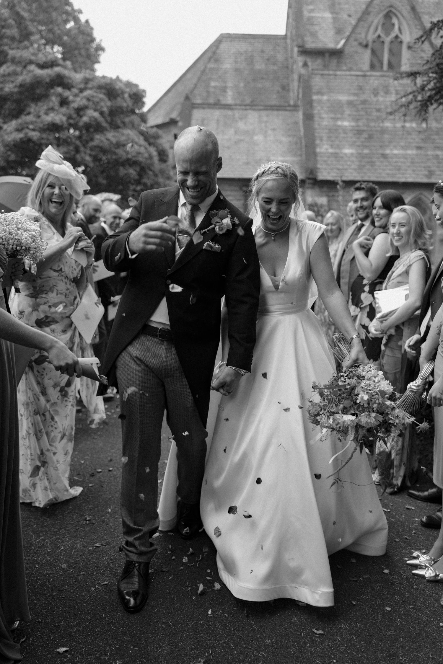 Black and white photo of wedding guests throwing confetti during outdoor celebration.