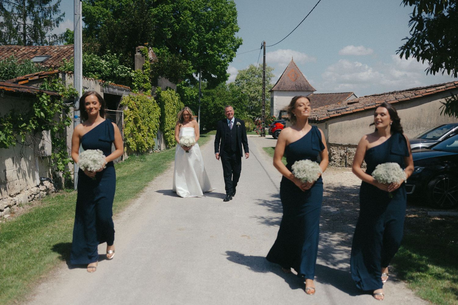 Wedding party in navy dresses walking along a garden path.