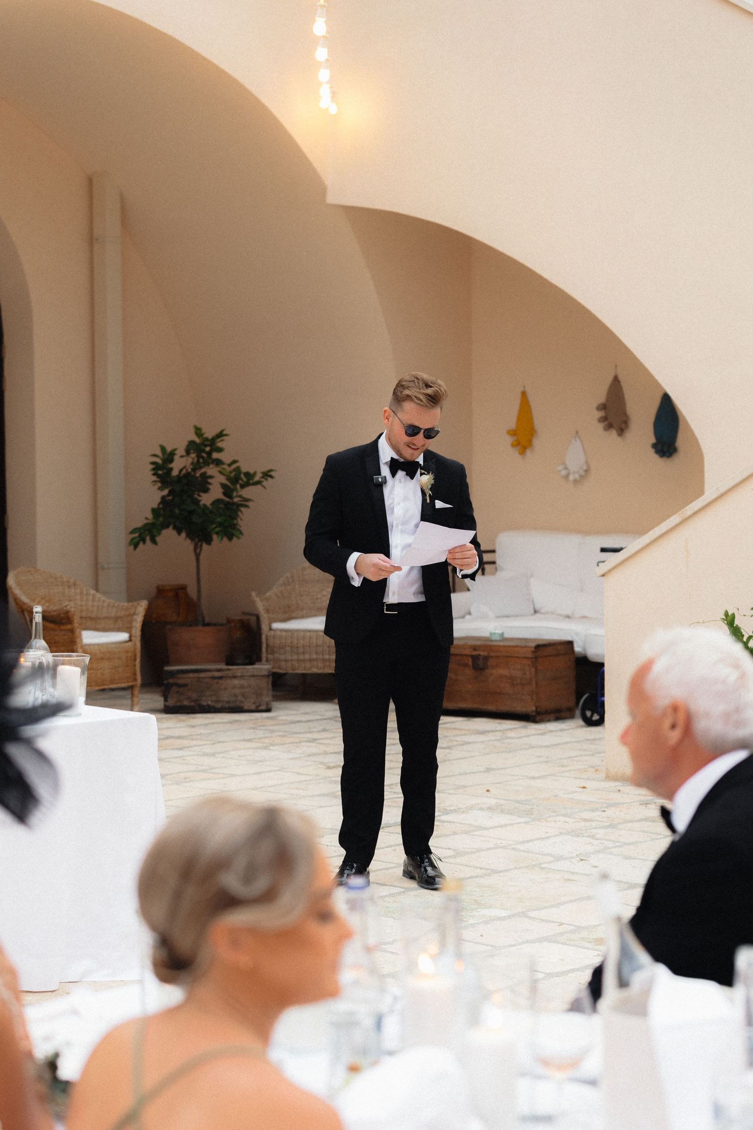 Speaker delivering a speech at an elegant wedding reception under arched ceilings.