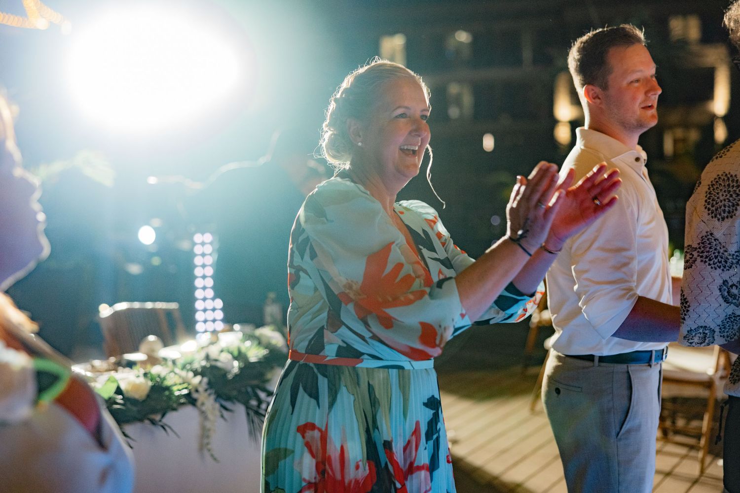 Couples dancing together at a dimly lit evening wedding reception with bright spotlights.